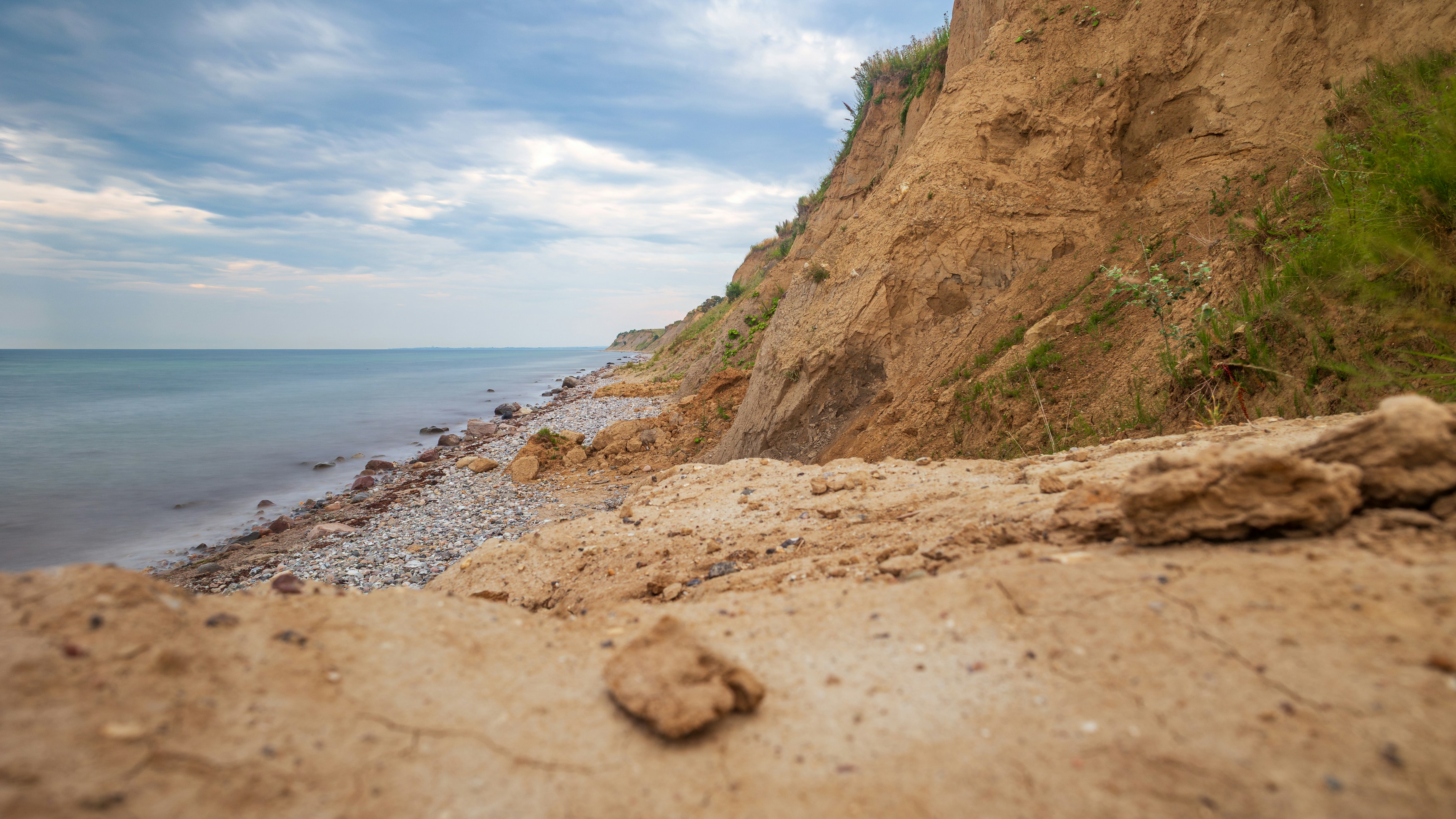 Sandy cliff overlooking the calm ocean under a cloudy sky