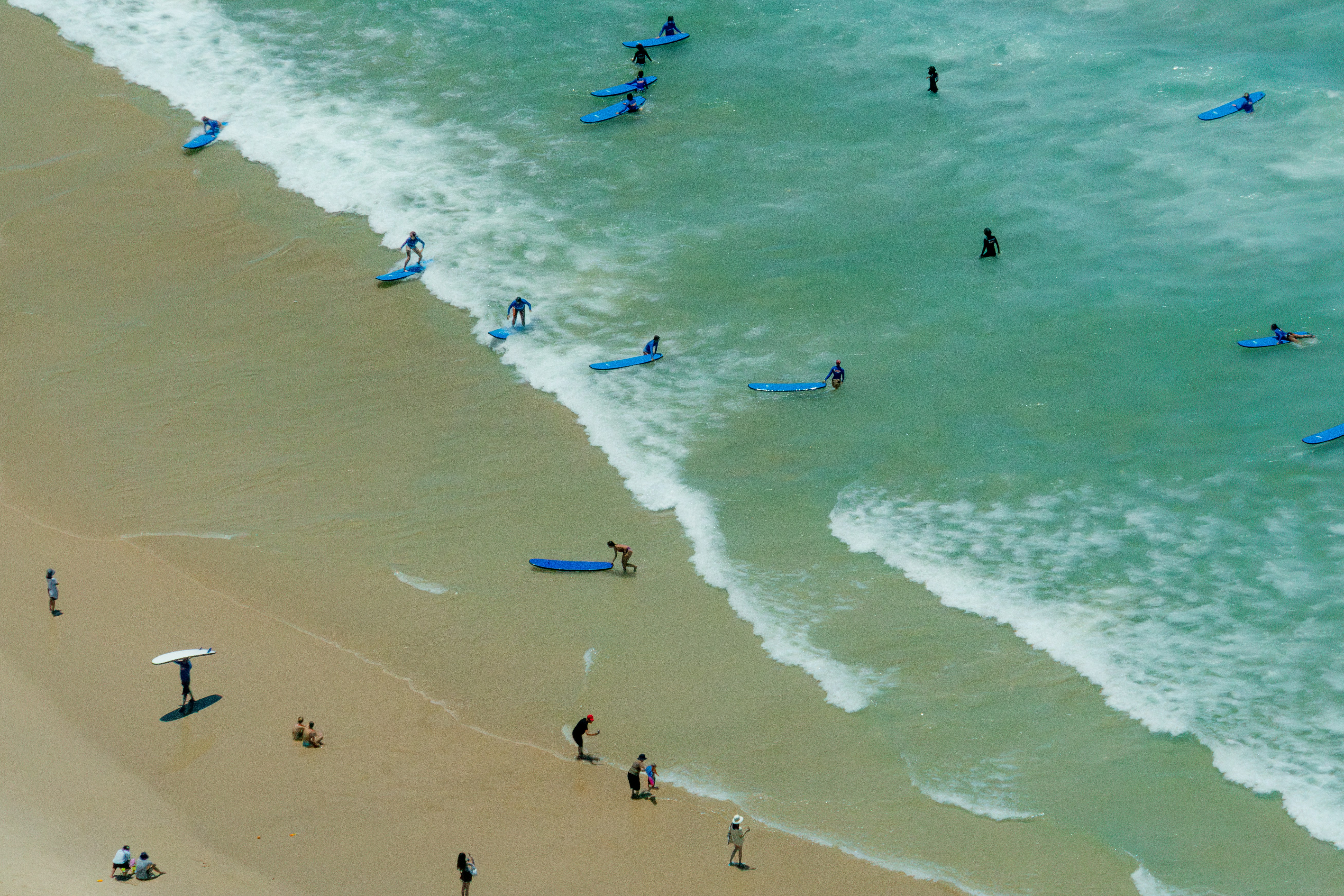 Surfers and beachgoers enjoying the sunny ocean waves.