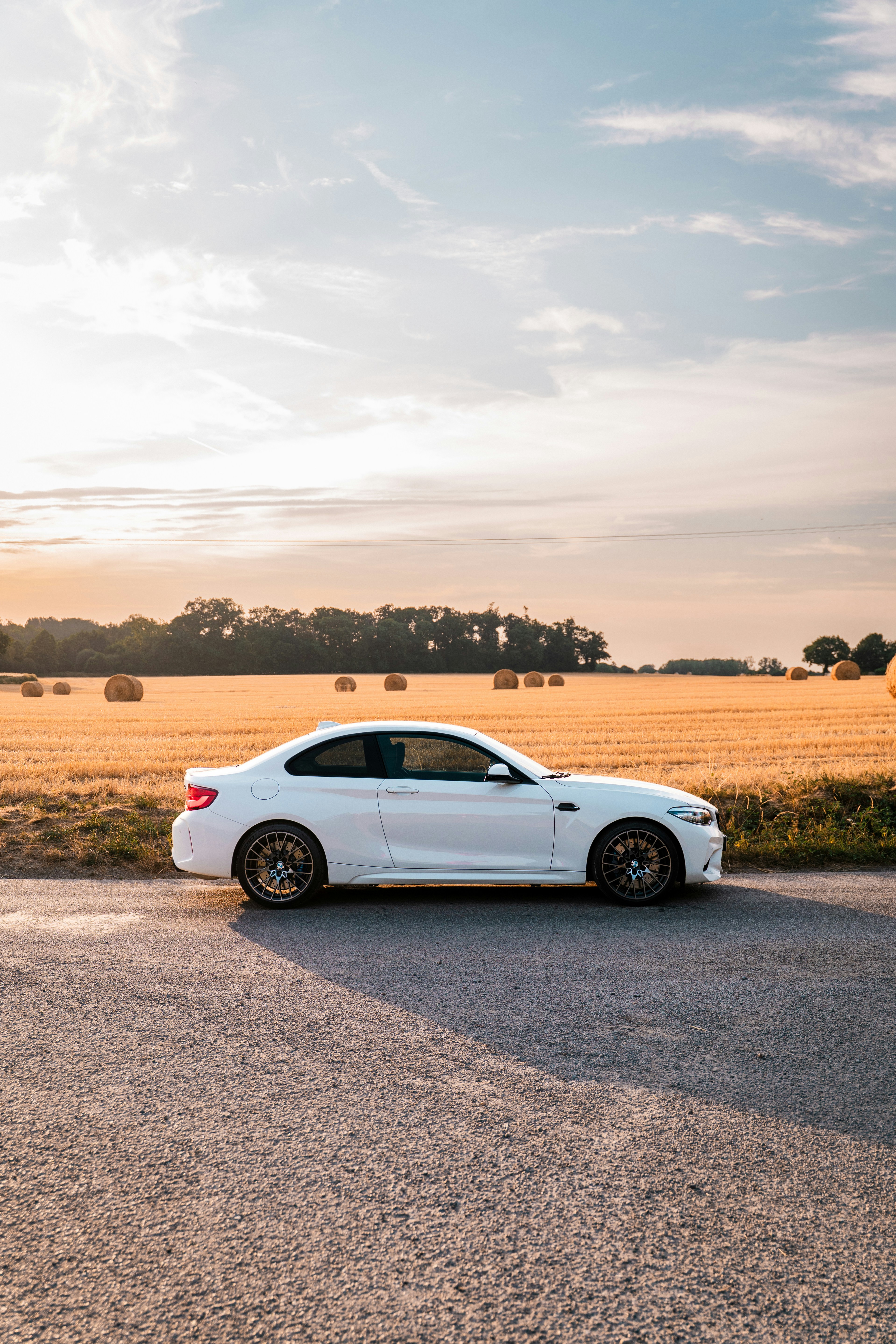 White sports car parked by a field of hay bales.