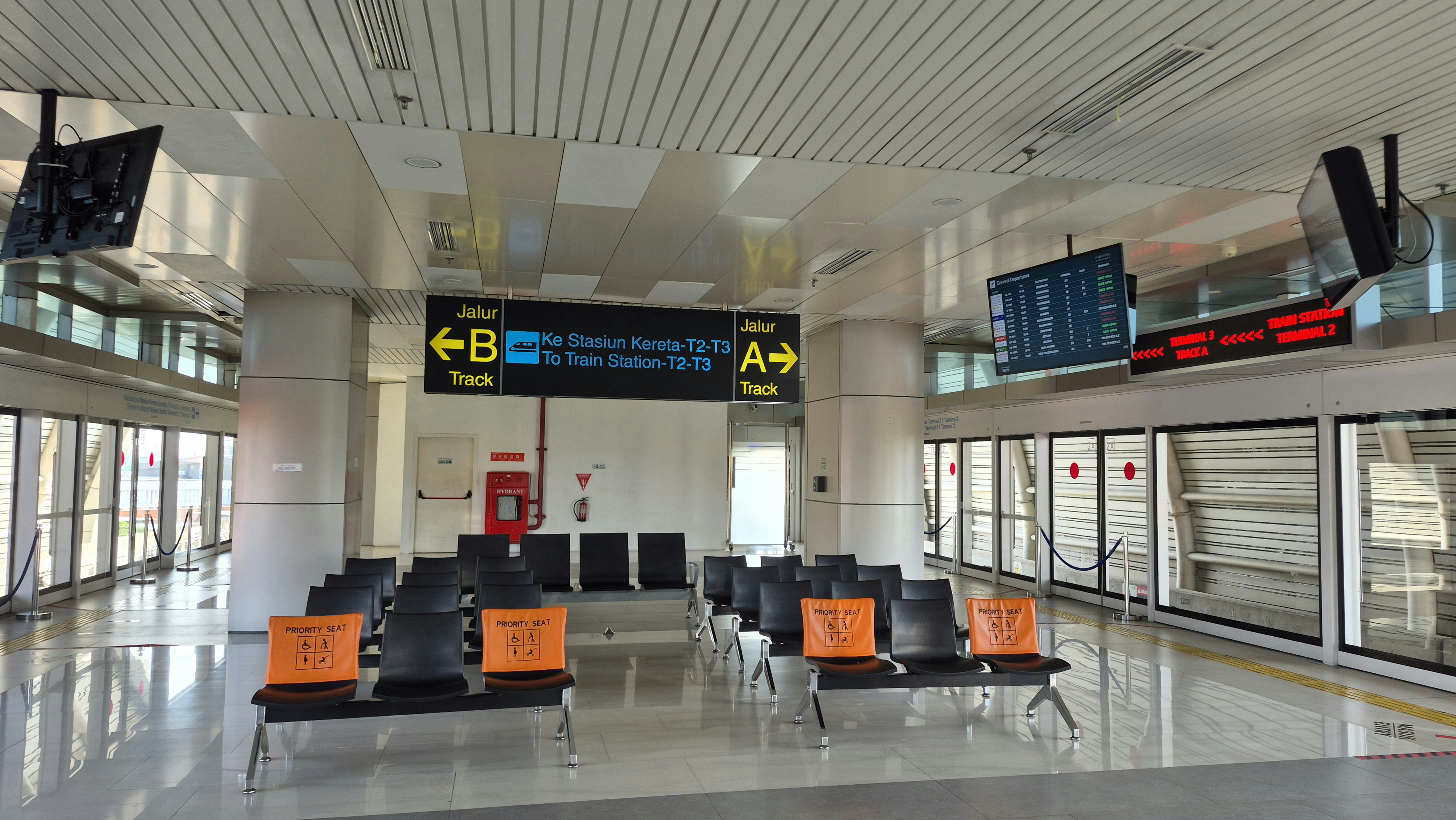 Área de espera vazia do aeroporto com assentos e displays digitais.