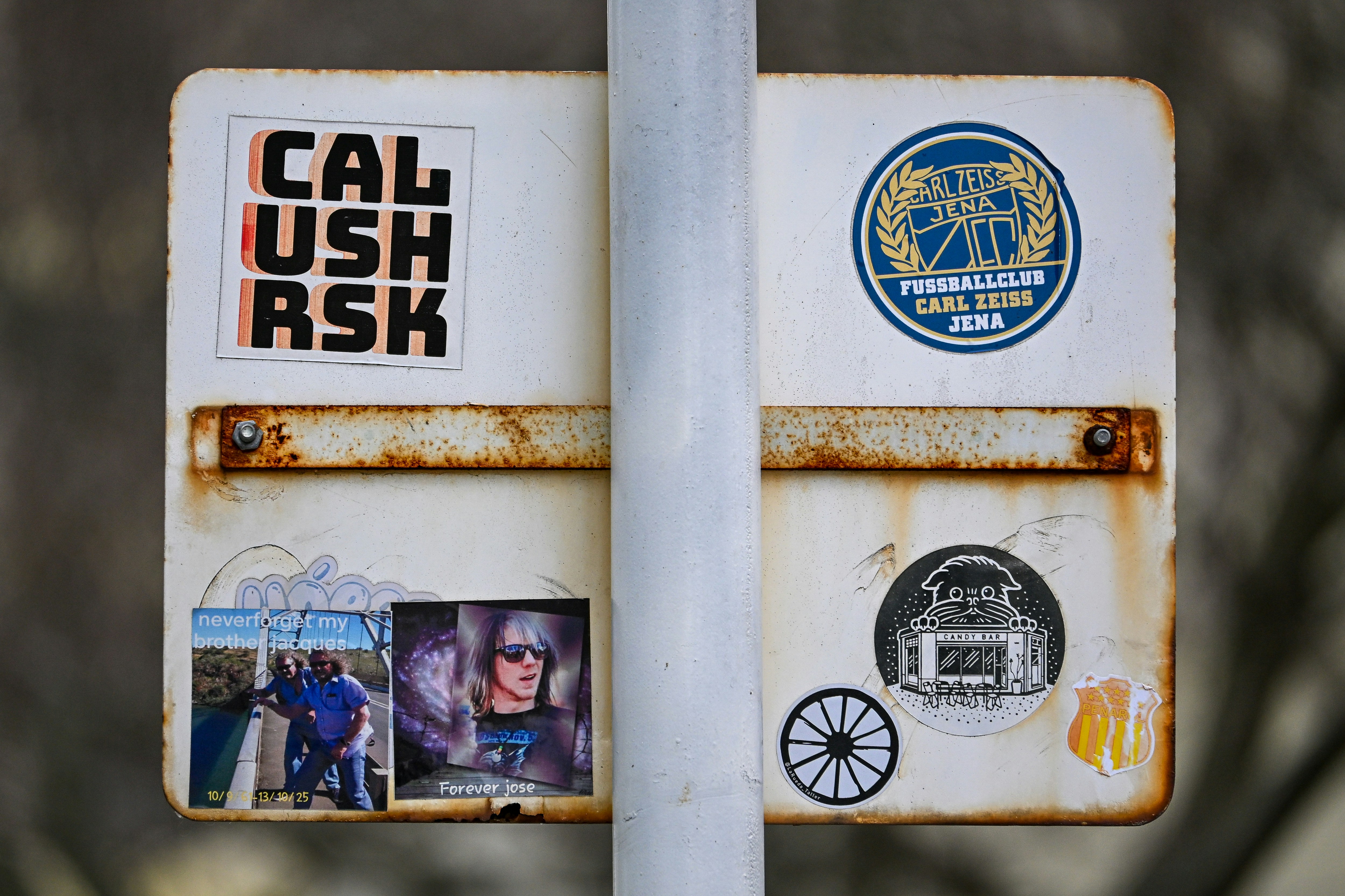 A rusty white signpost covered with various stickers.