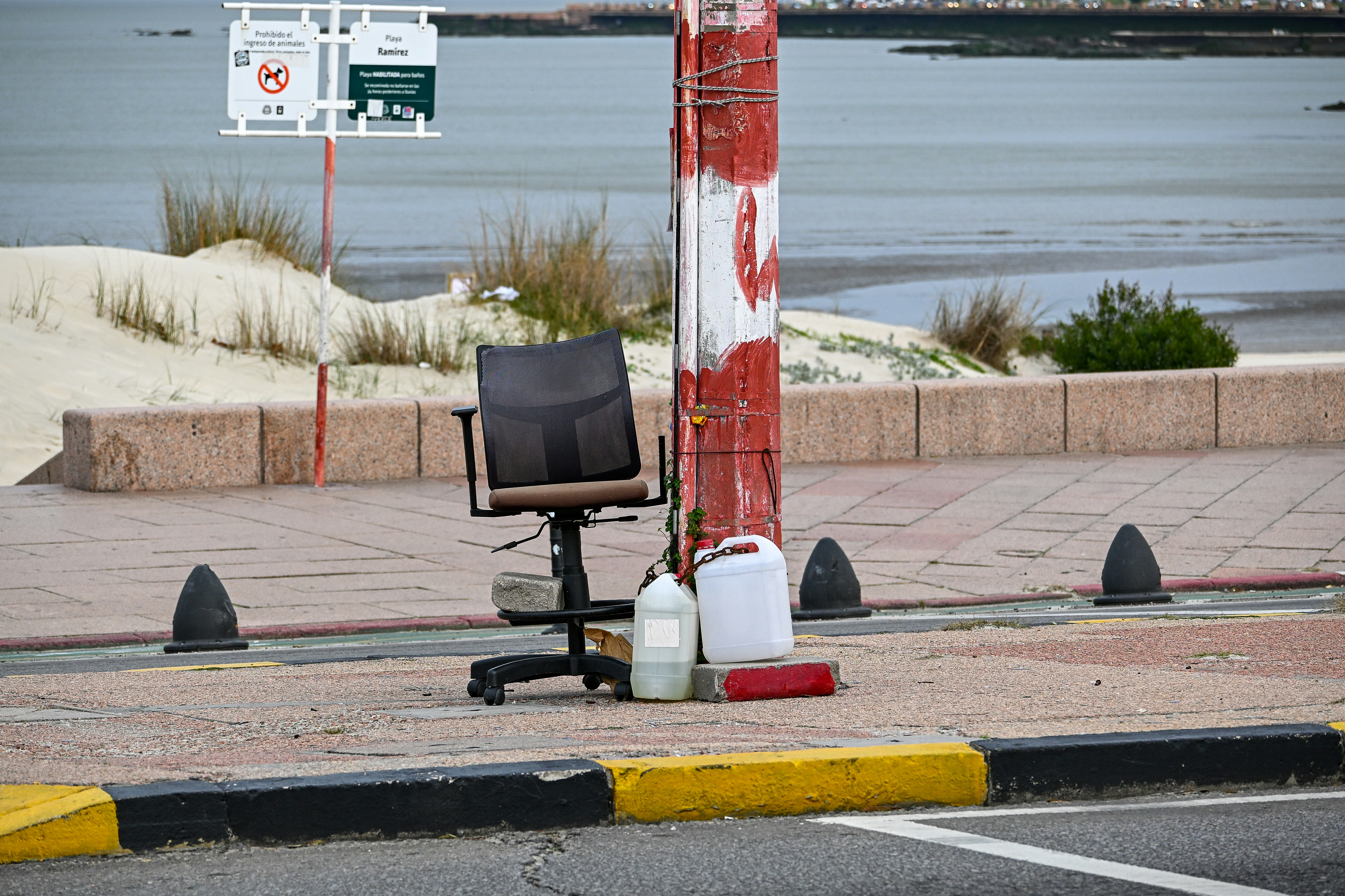 Office chair, containers, and striped pole on pavement near beach.
