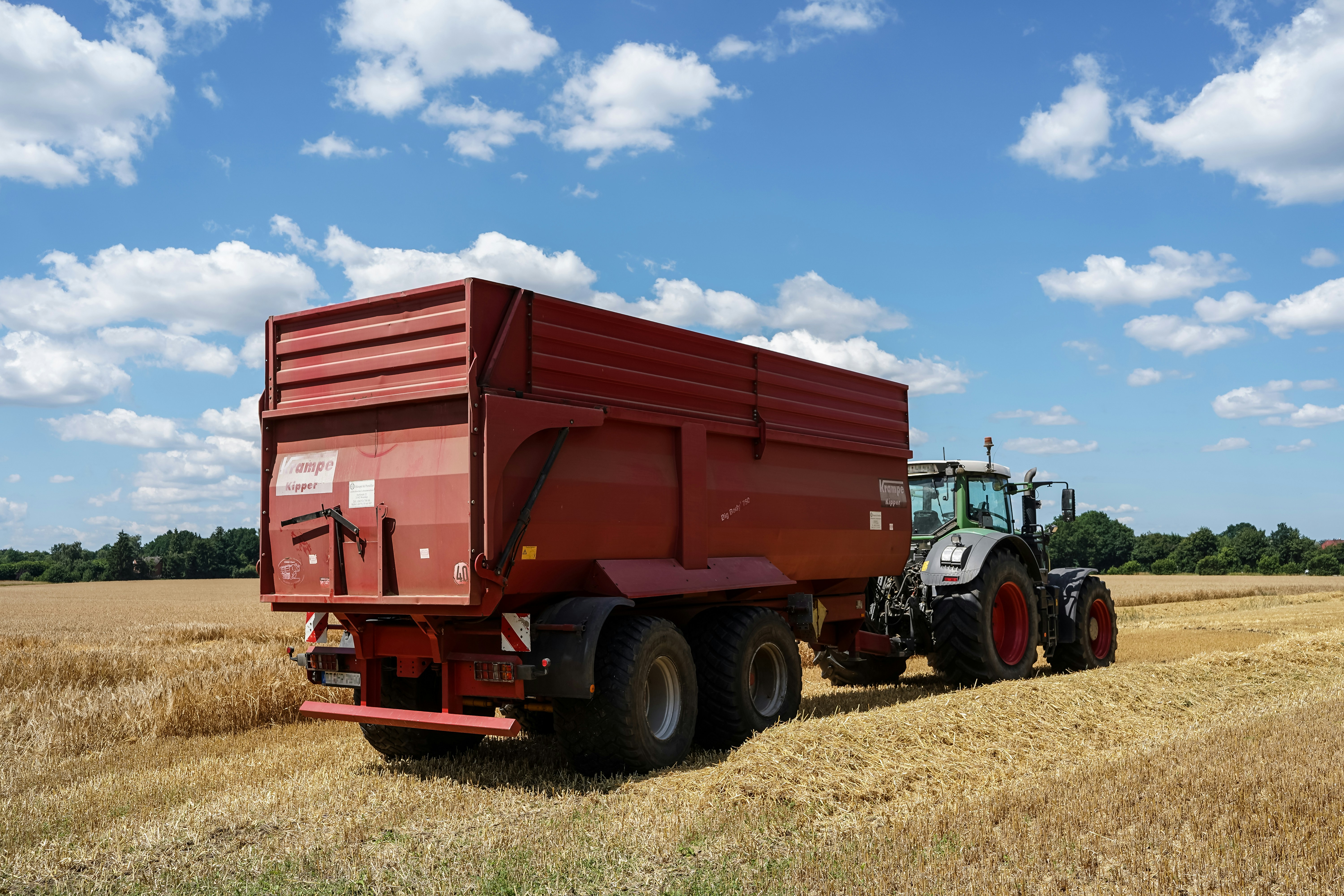 Trator agrícola puxando um grande trailer vermelho no campo.