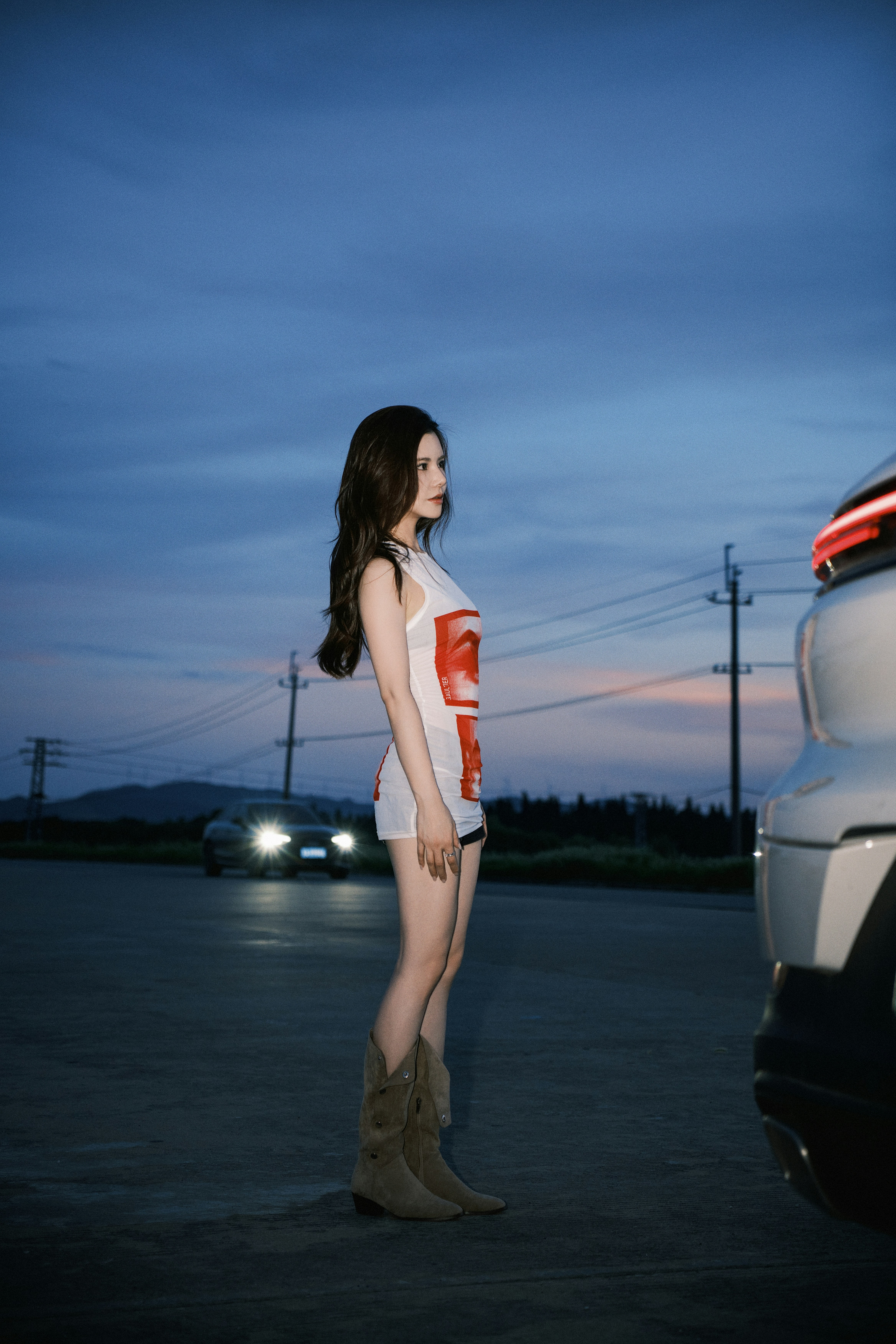 Young woman standing by a car at dusk