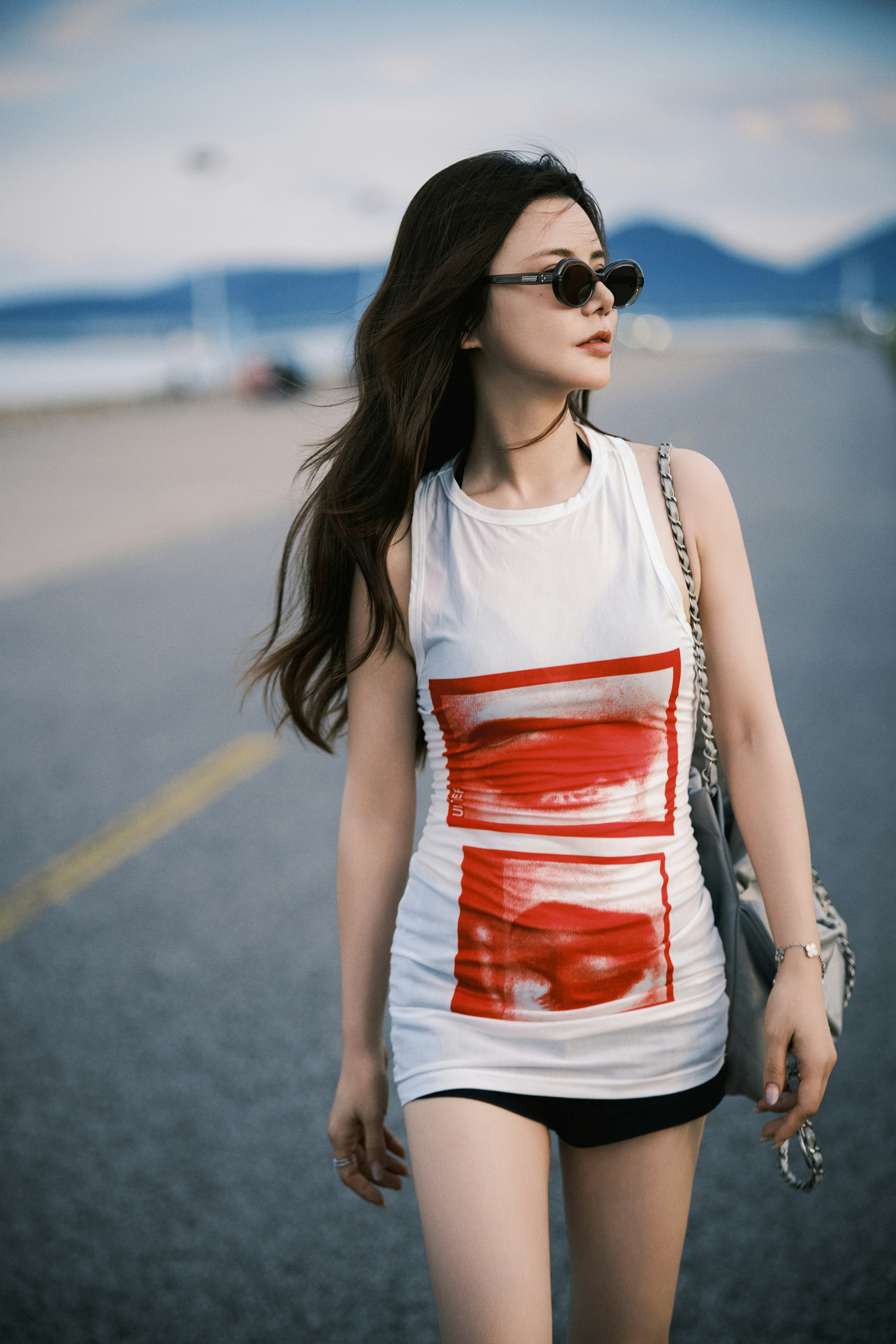 Woman in white top and sunglasses walks on coastal road