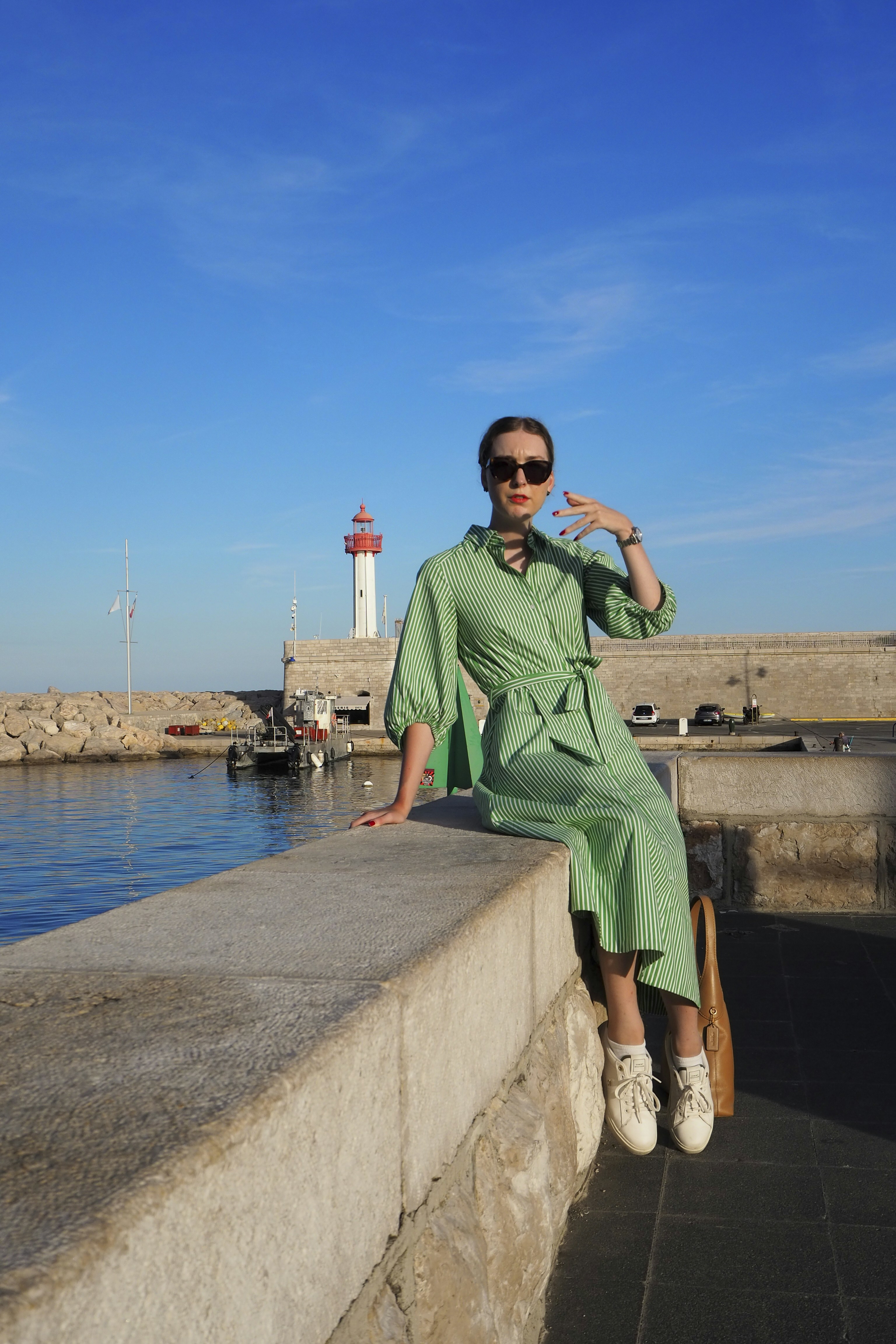 Donna alla moda in abito verde vicino al porto con faro