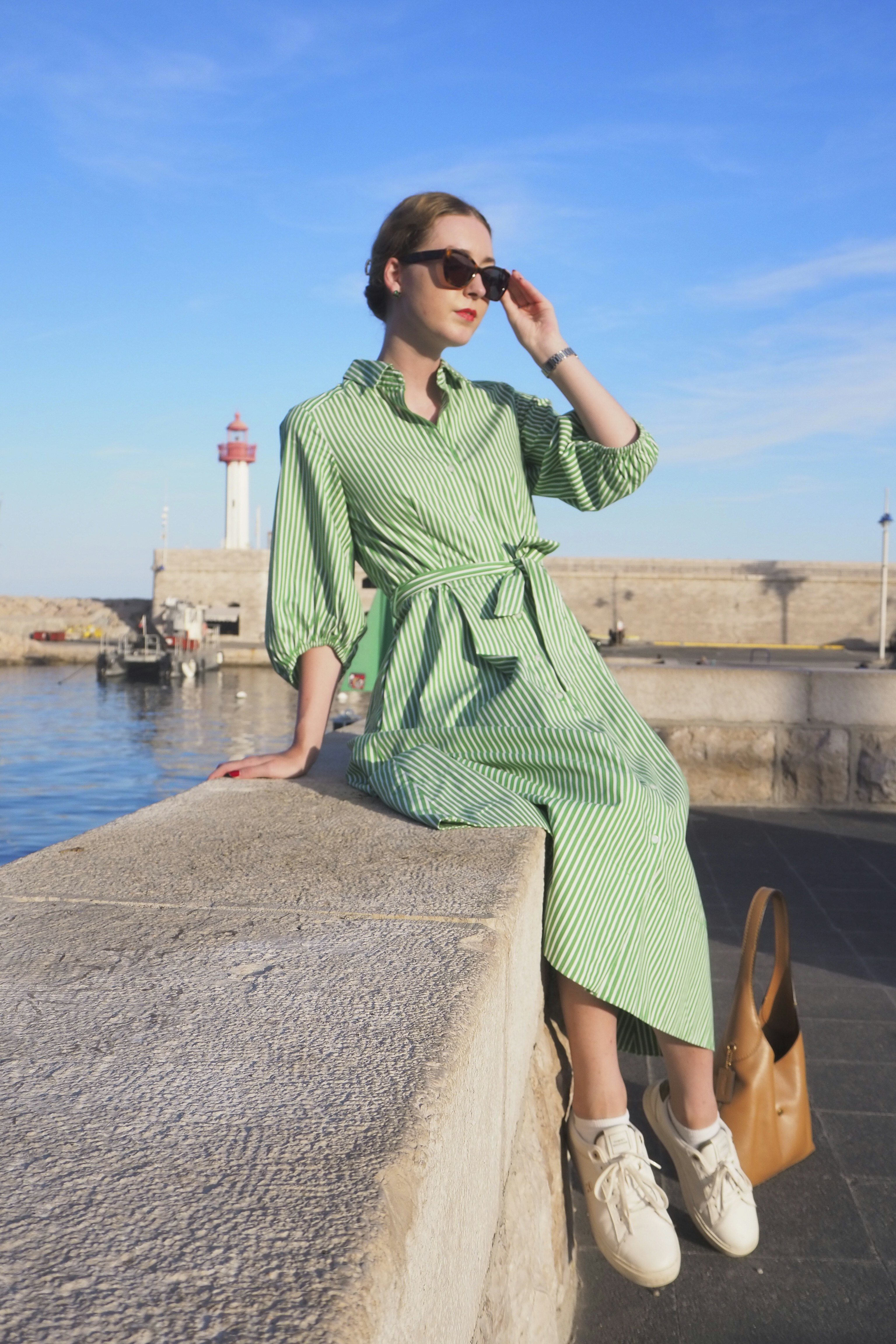 Woman in green striped dress sitting on a harbor wall