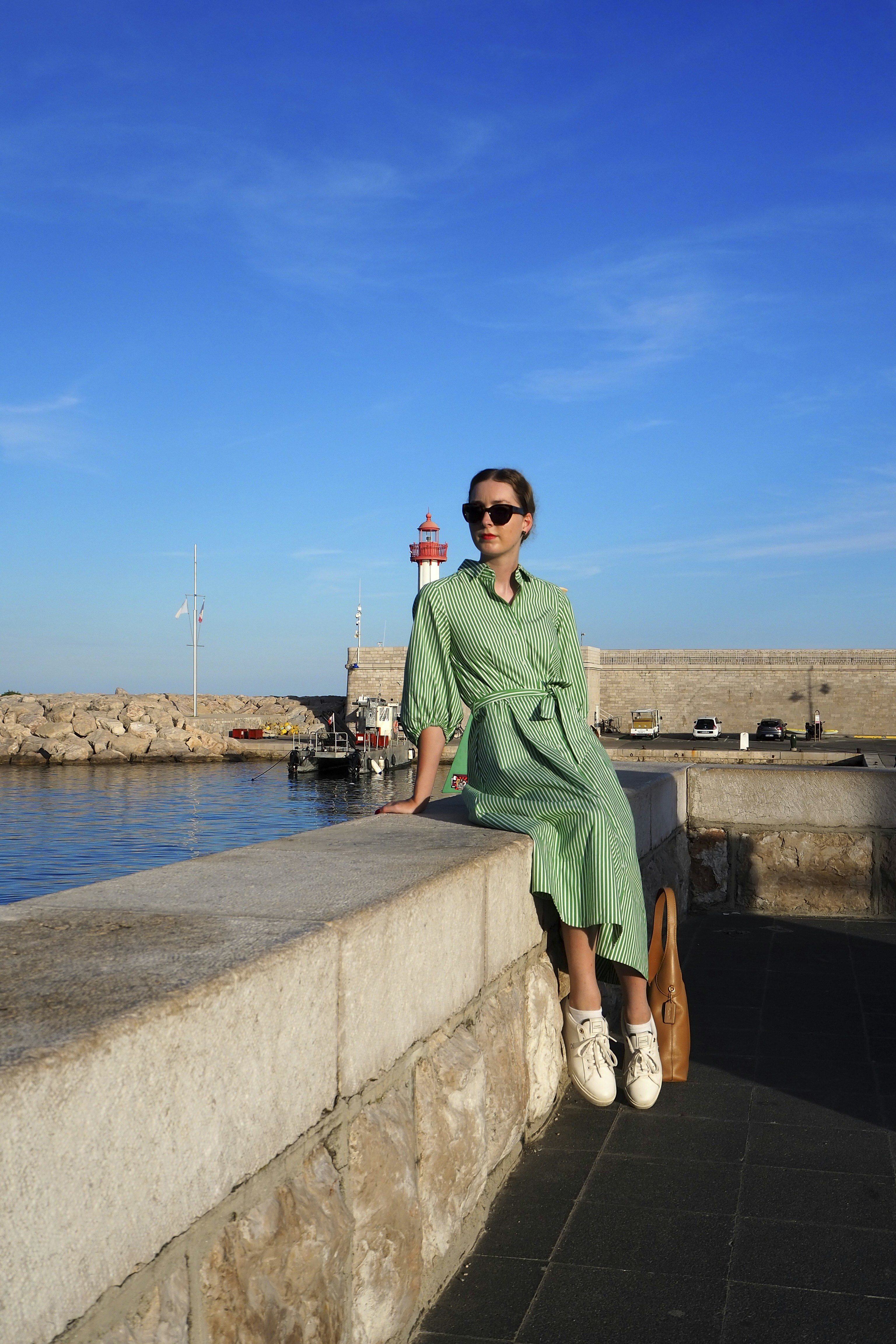 Donna in abito verde seduta su un muro vicino al porto