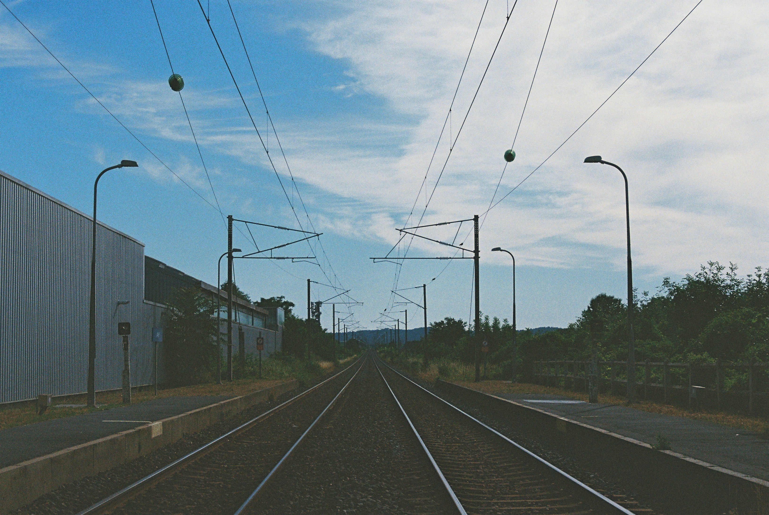 Railway tracks under power lines beside an industrial shed