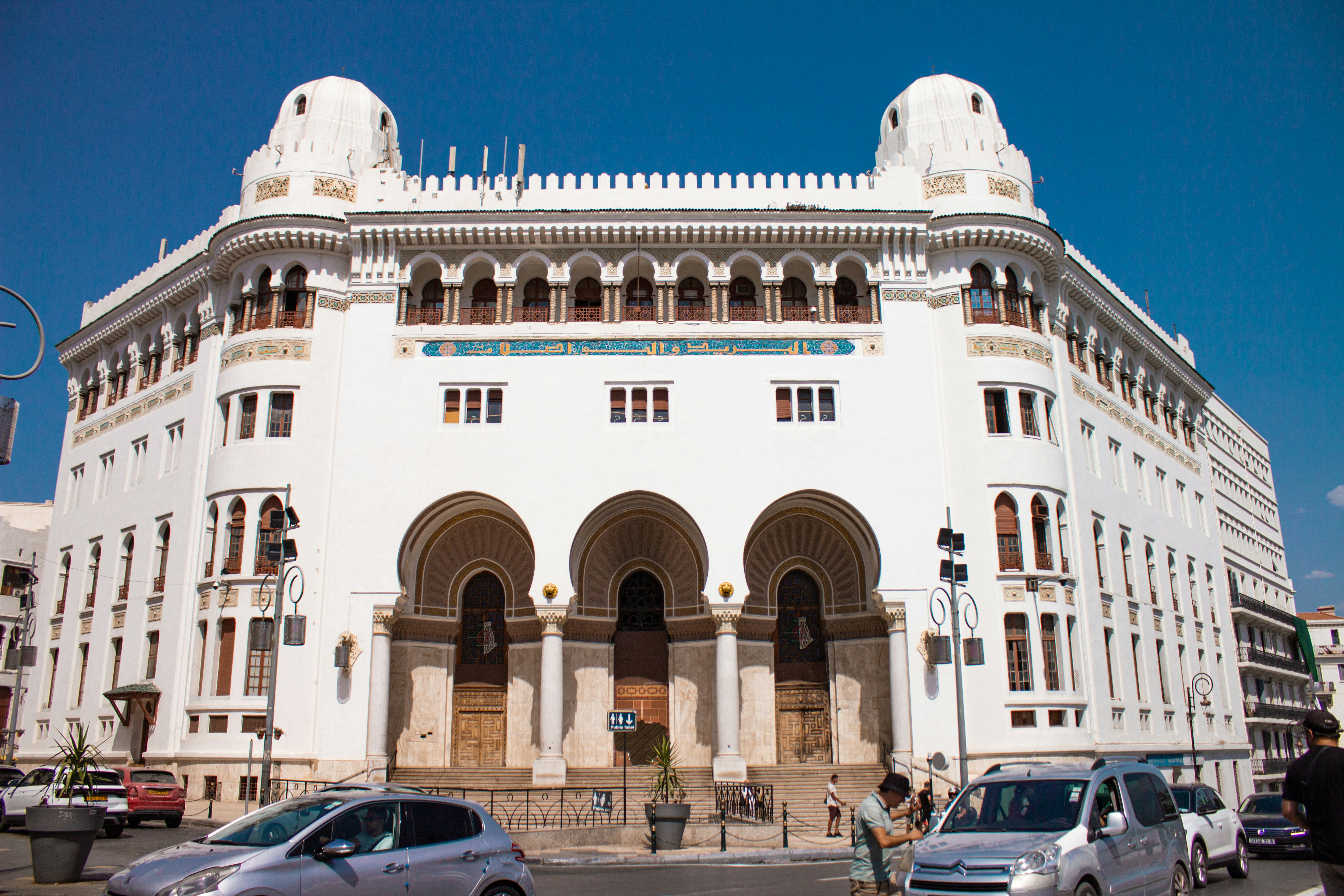 Ornate white building with arched entrances and street traffic.