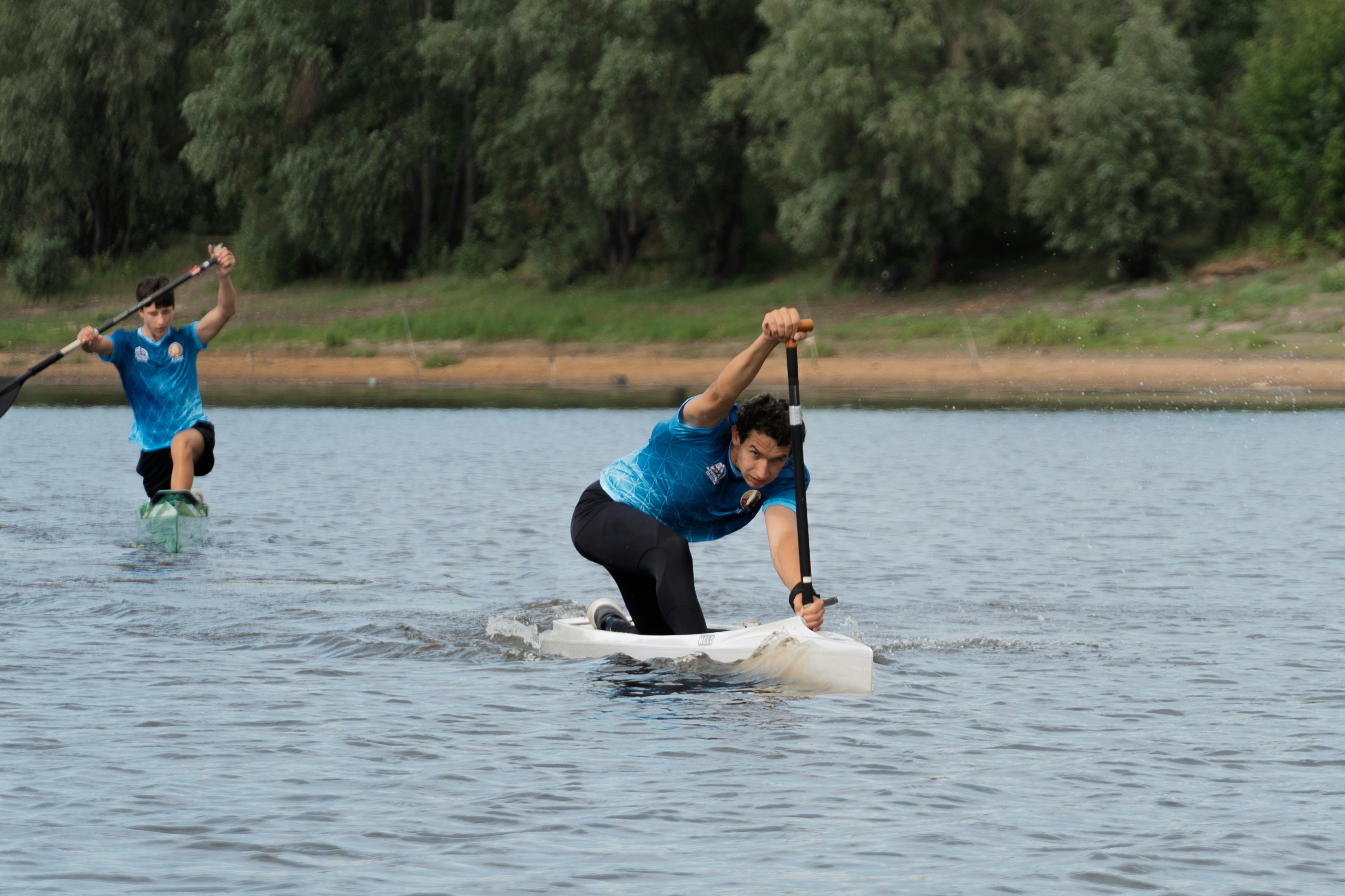 Two paddlers on water, one kneeling, one standing