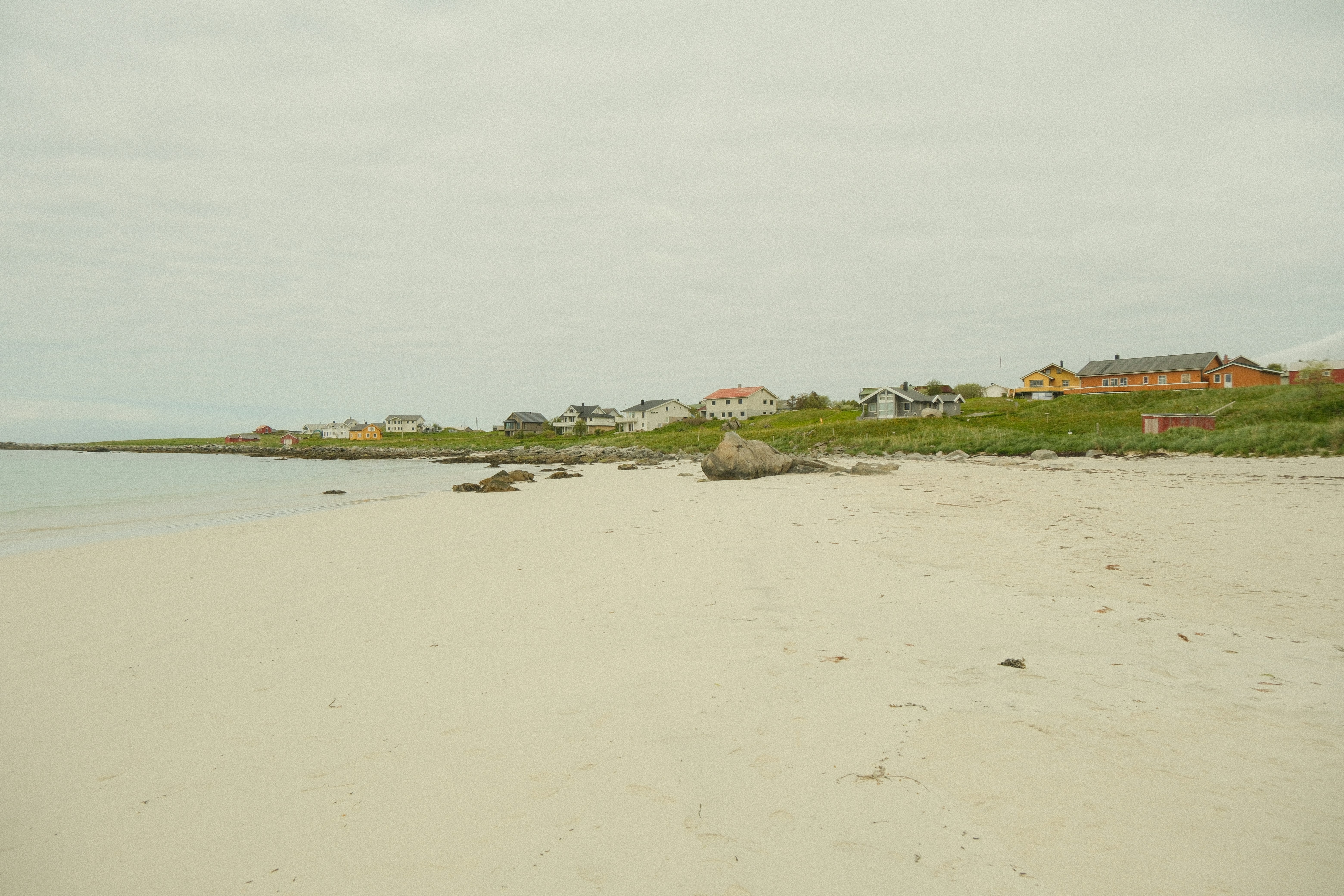 Sandy beach with scattered rocks and houses along the coastline.