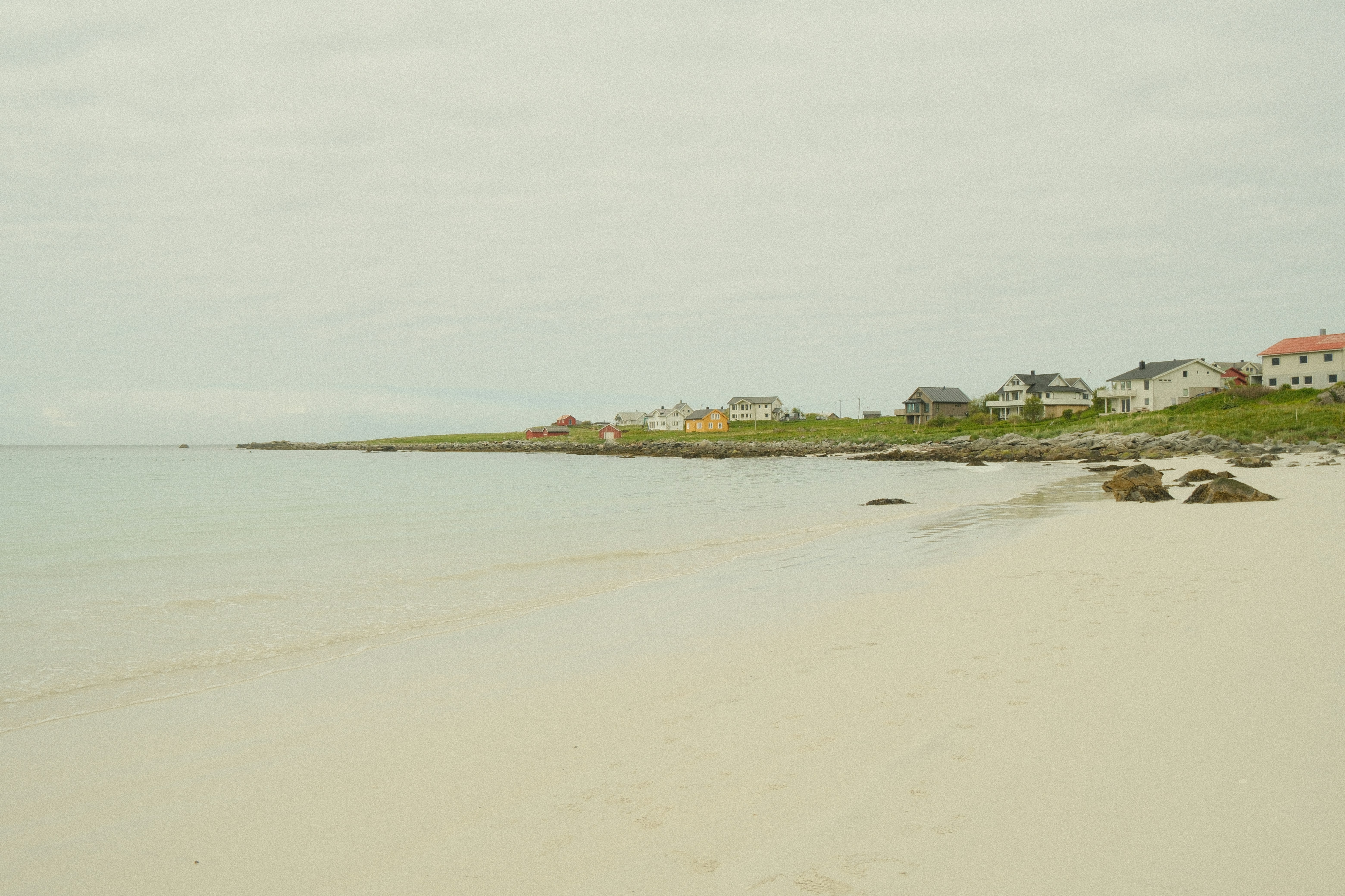 Coastal houses line a sandy beach under an overcast sky.