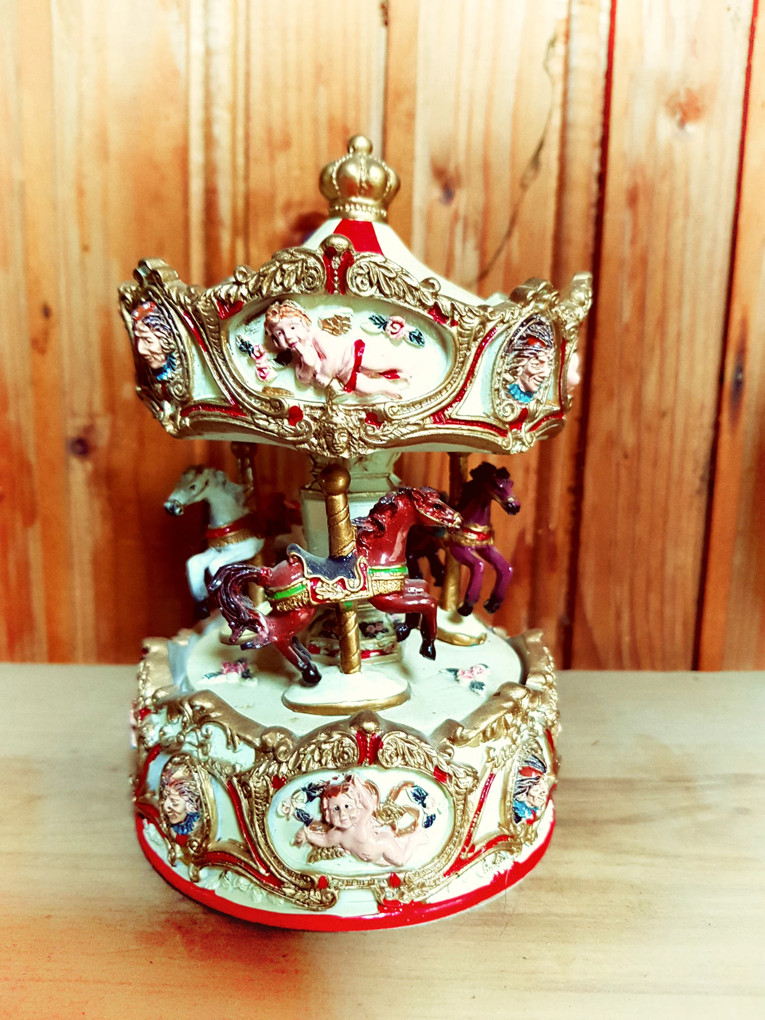 The Gilded Carousel music box: painted horses circling under a gilt and red canopy on a wooden shelf
