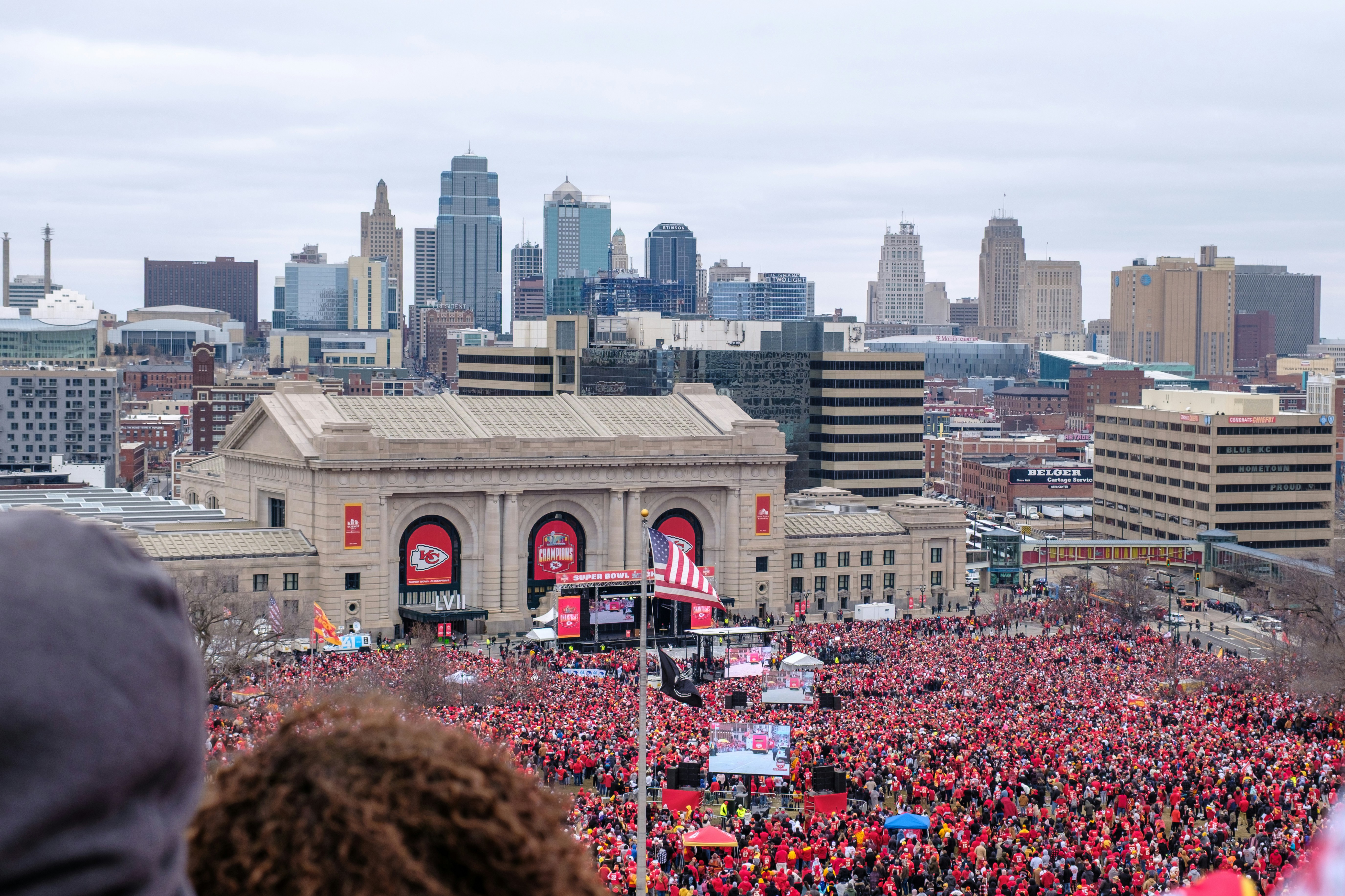 Red-clad crowd gathers for an event before a city skyline.