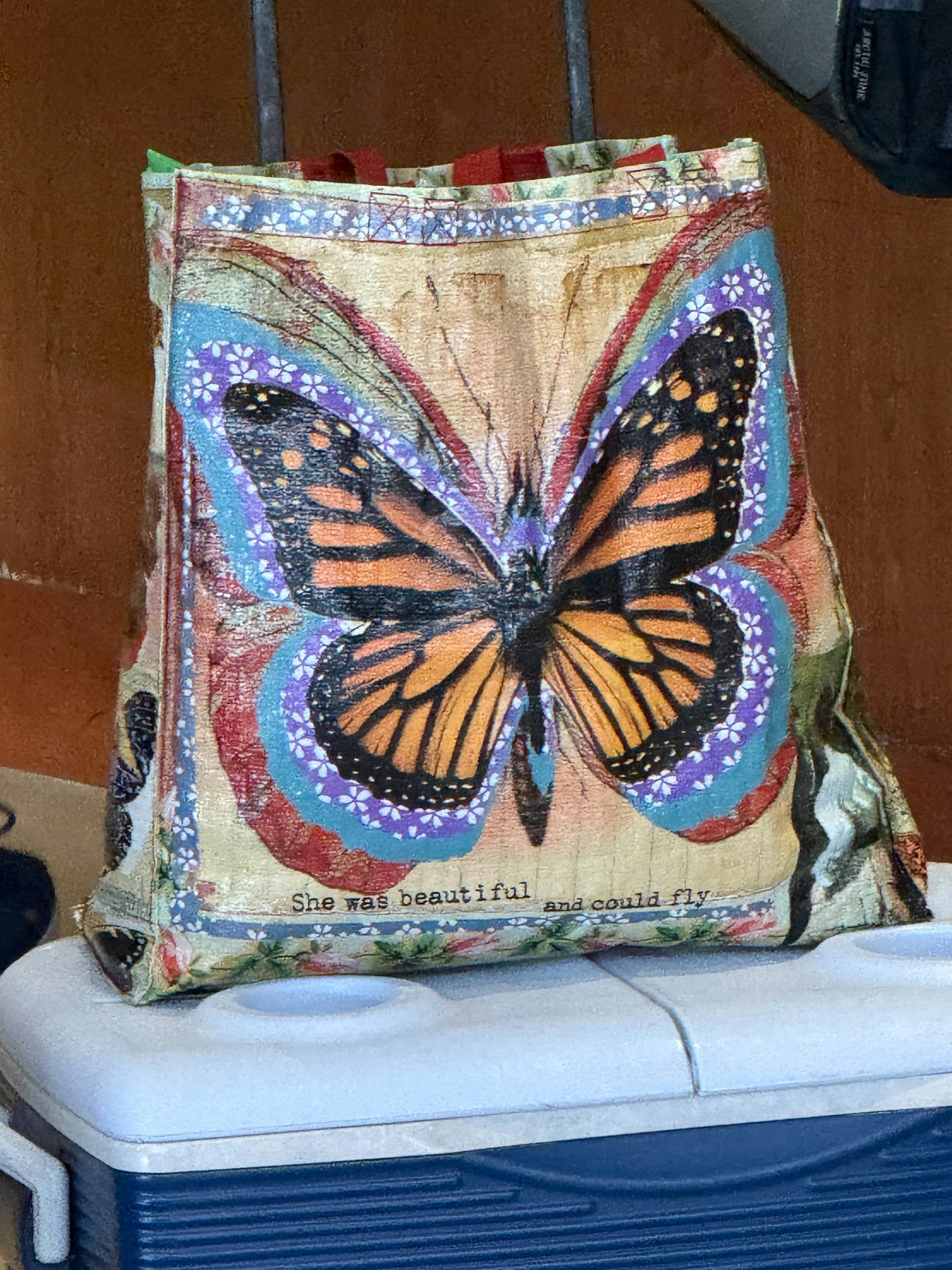 A butterfly-themed reusable bag rests on a white cooler.