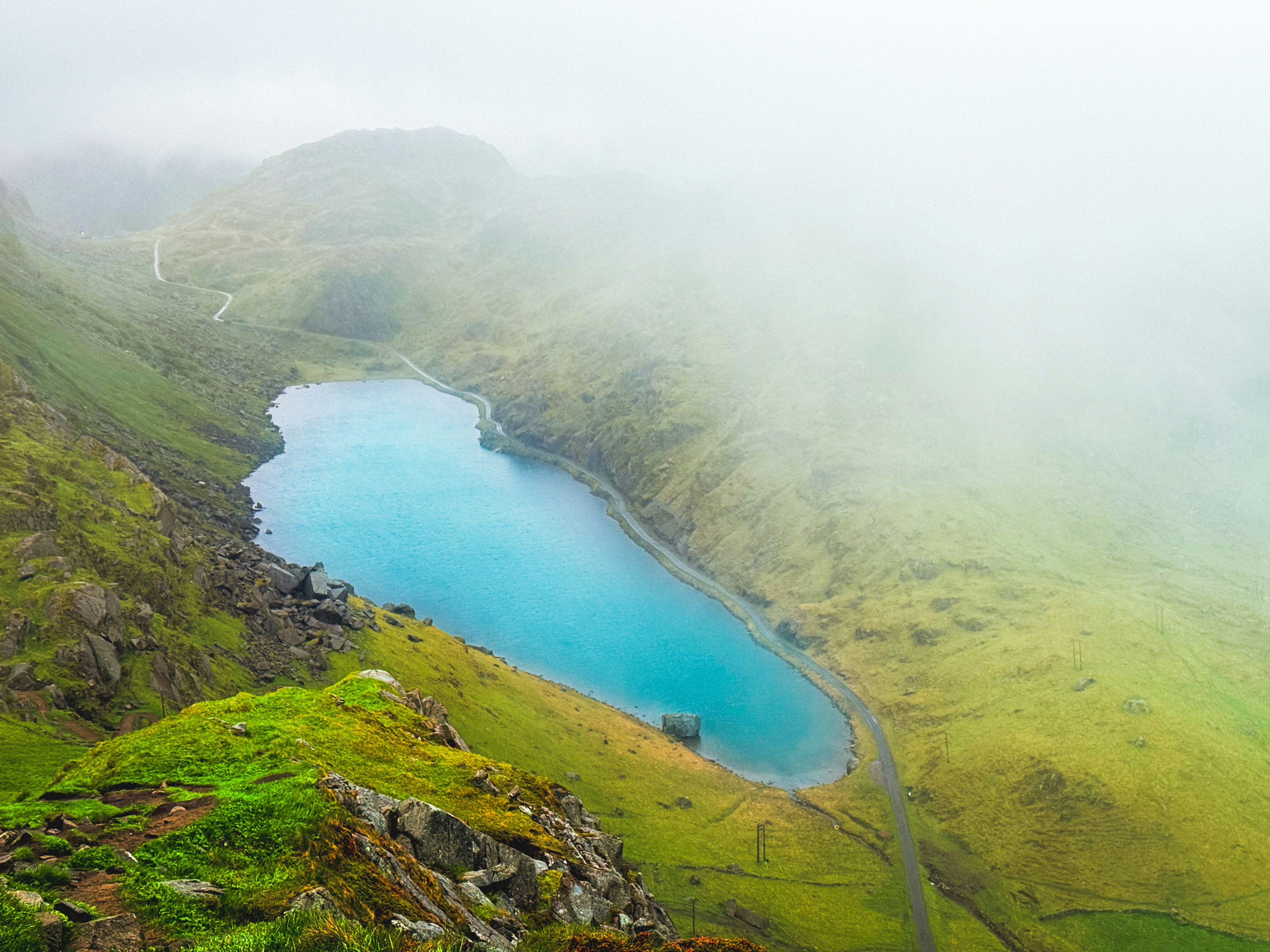 A vibrant blue lake surrounded by green mountains and mist