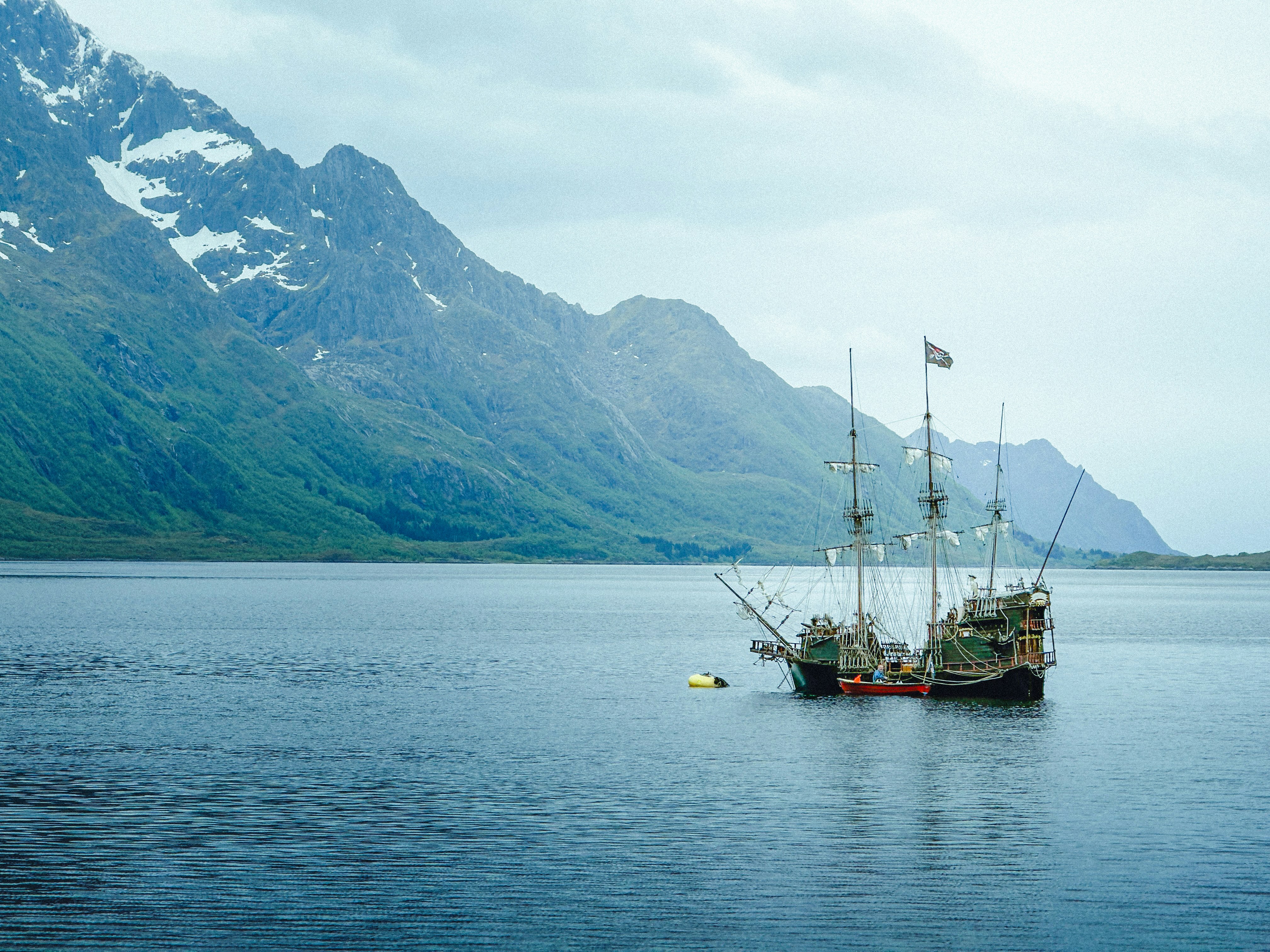 A tall ship anchored in a calm bay with mountains
