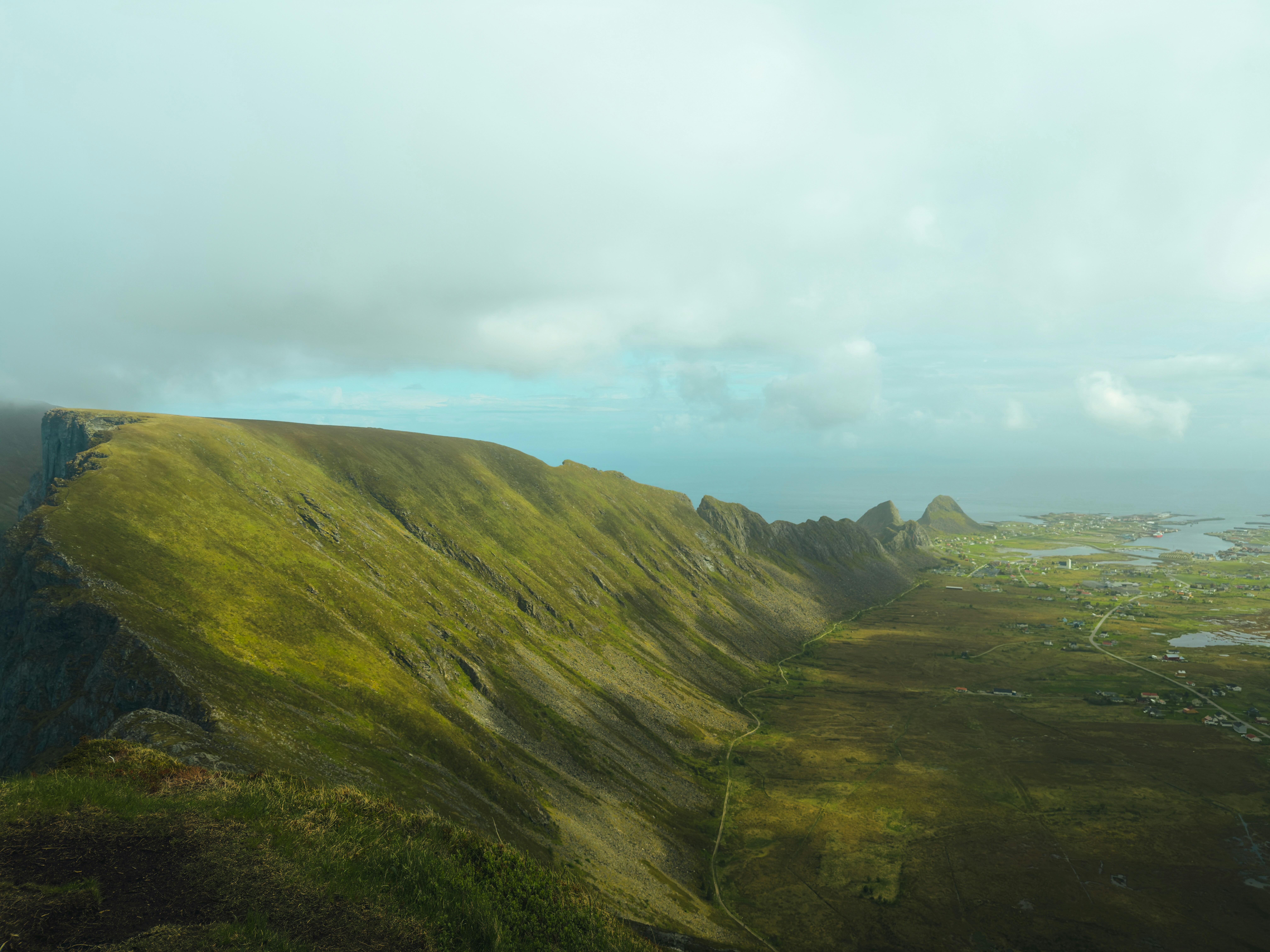 Green mountain landscape with distant settlement under a cloudy sky
