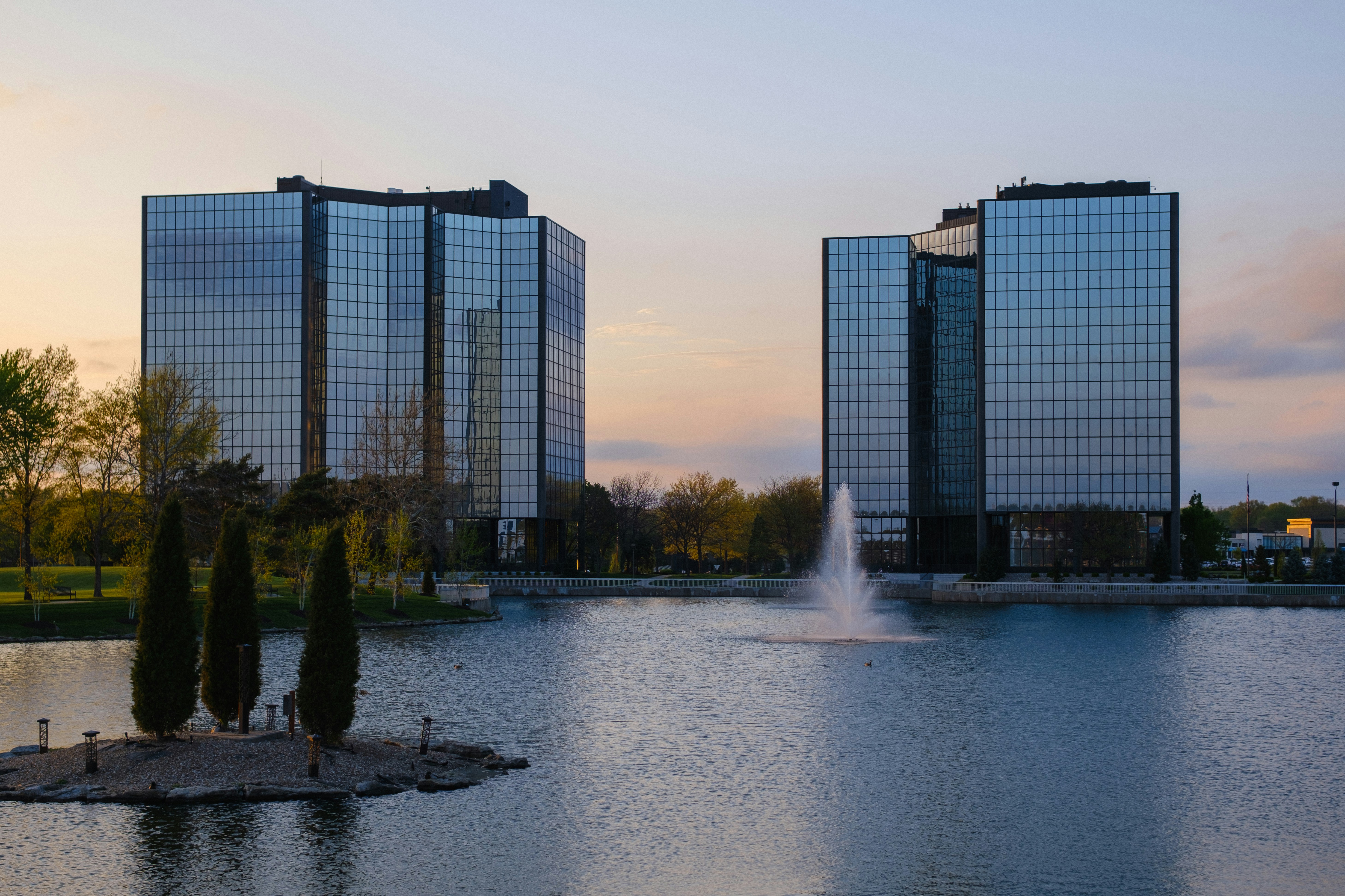 Glass buildings and a lake with a fountain at dusk.