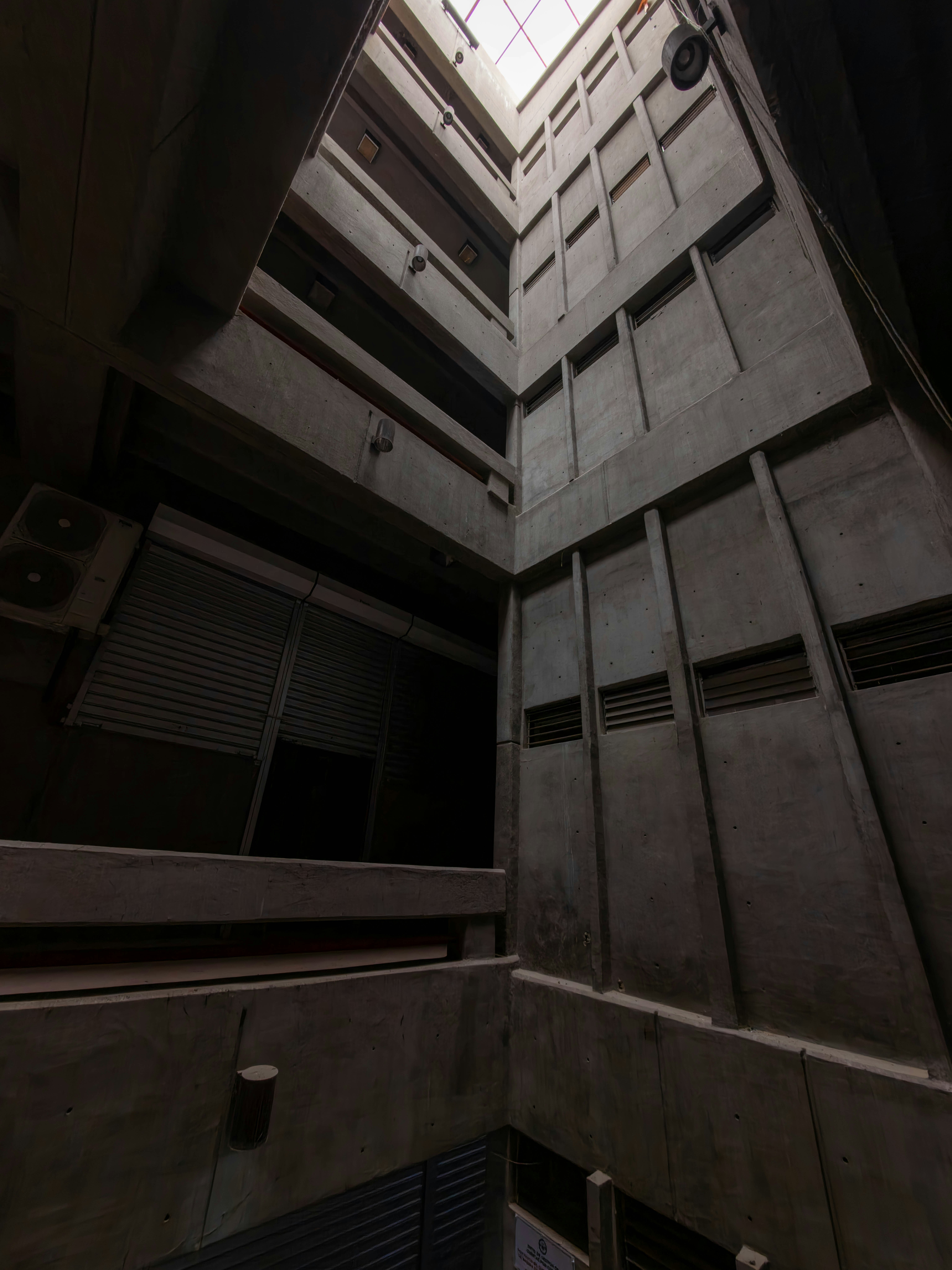 Dark concrete building interior looking up towards a skylight.