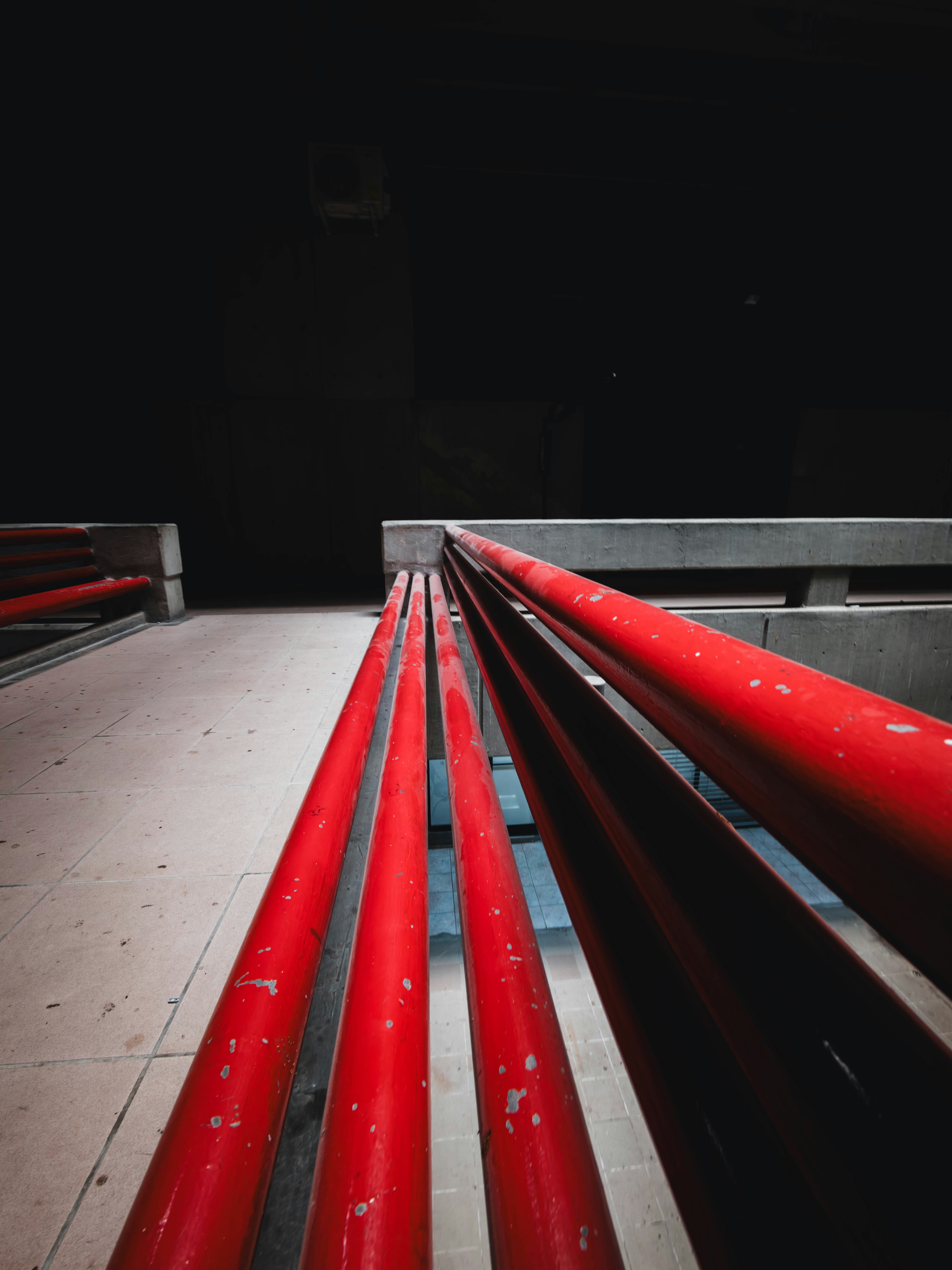 Industrial red railing lines recede toward a dark vanishing point, emphasizing perspective on a concrete platform and empty space beyond. This is a documentary-style capture of an architectural moment.