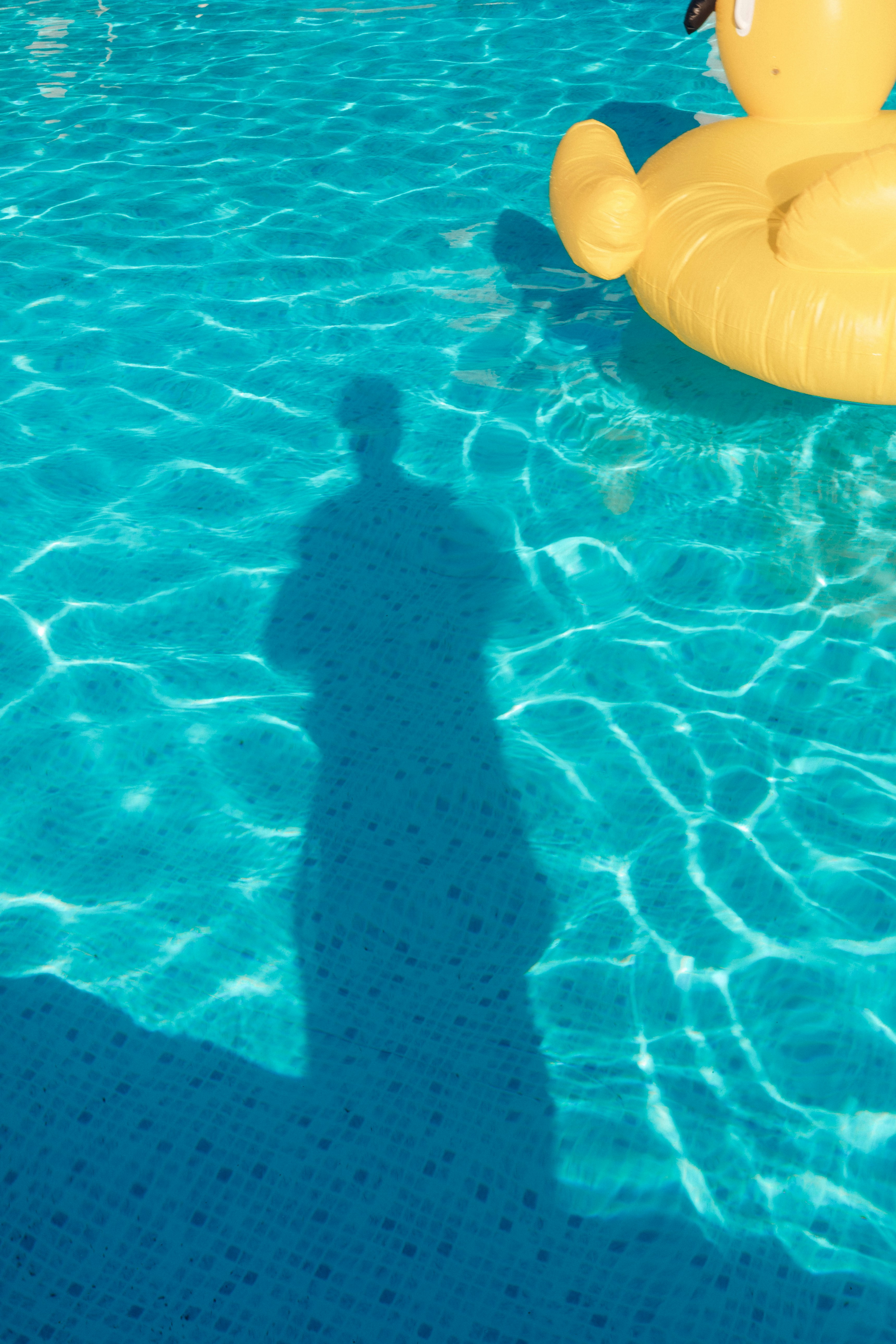 Person's shadow and yellow duck in a blue swimming pool.