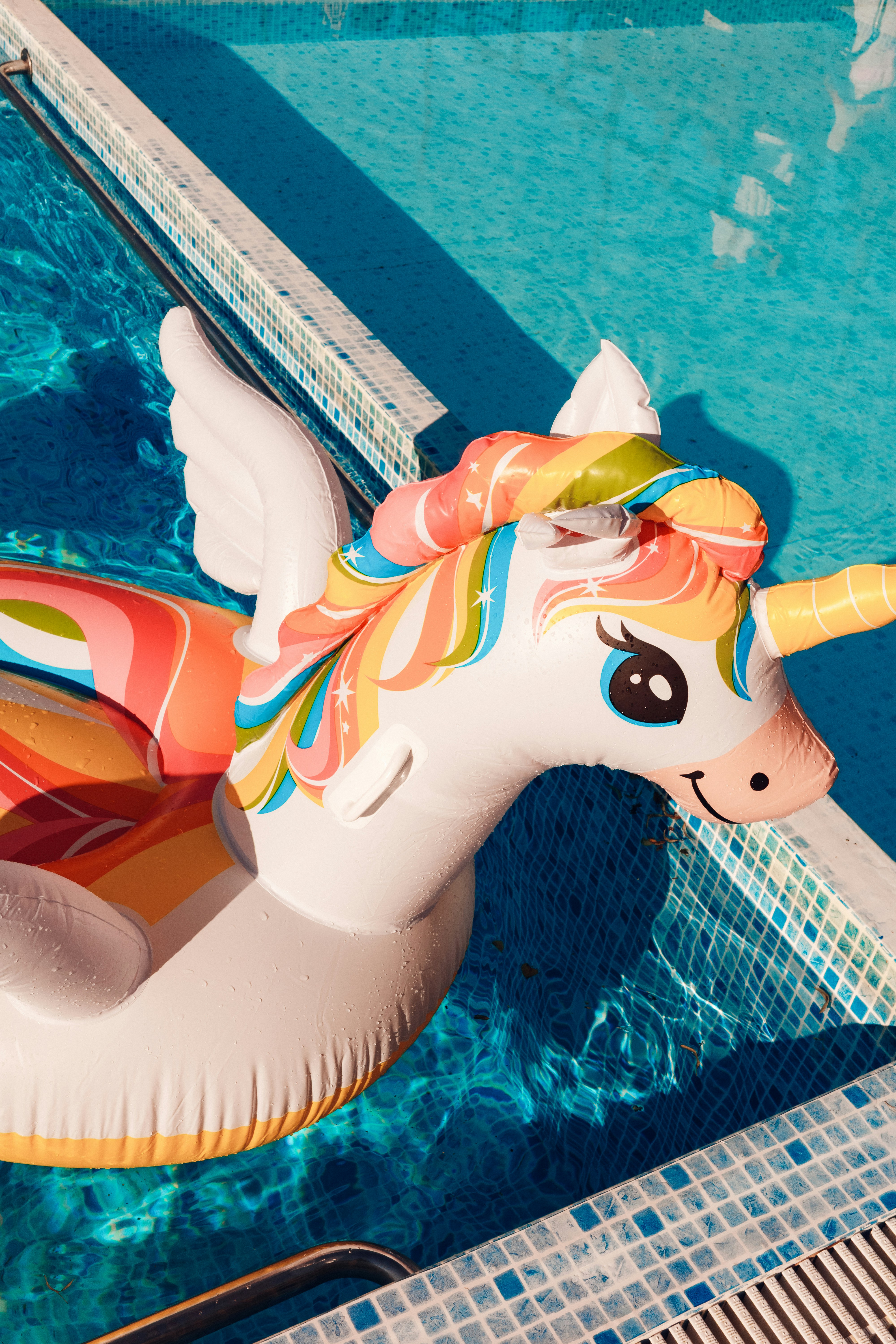 A colorful inflatable unicorn floats in a blue swimming pool.