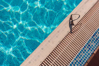 Swimming goggles resting on the edge of a blue pool.