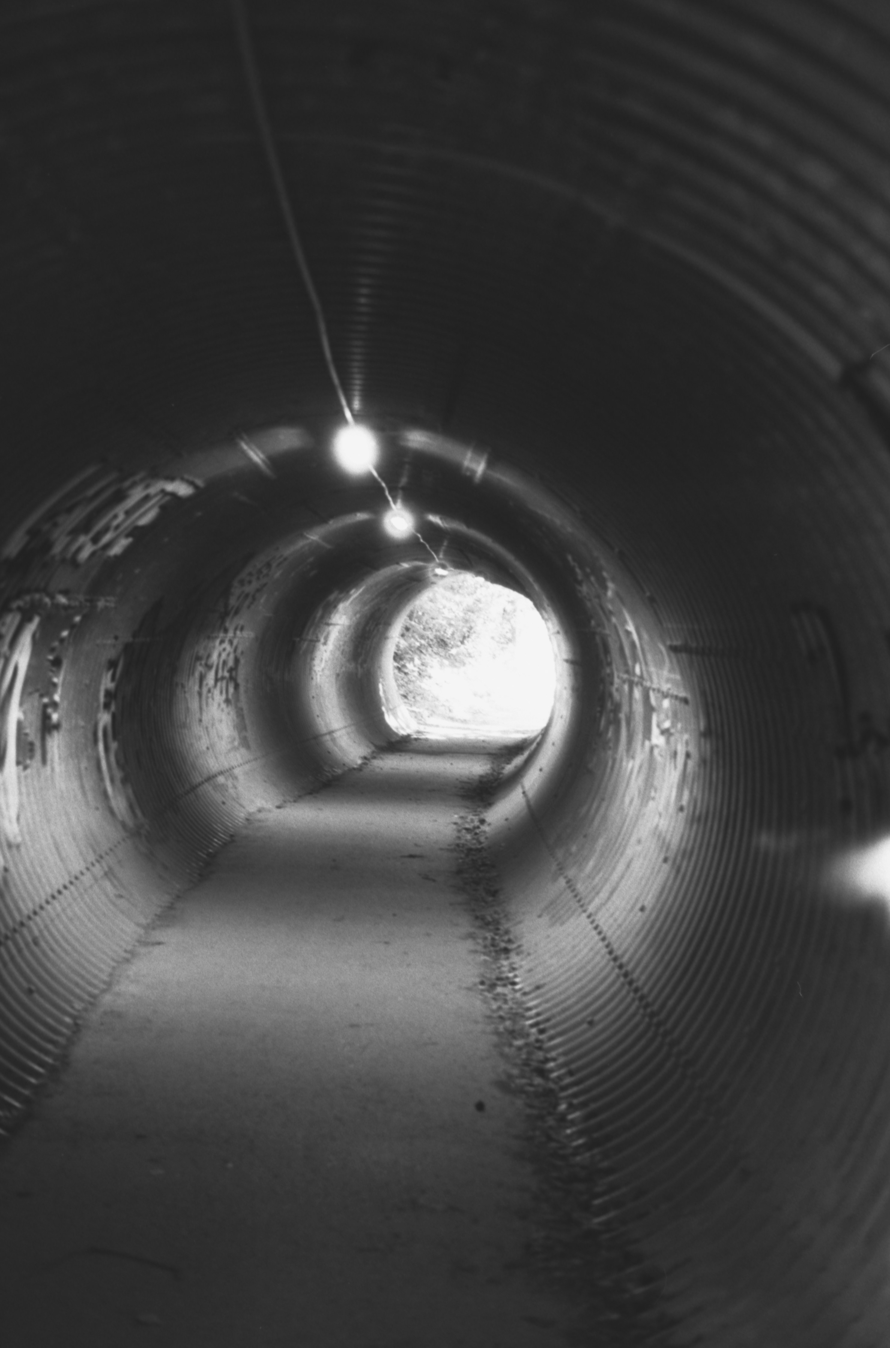 Tunnel scuro in lamiera ondulata con luci e uscita luminosa.