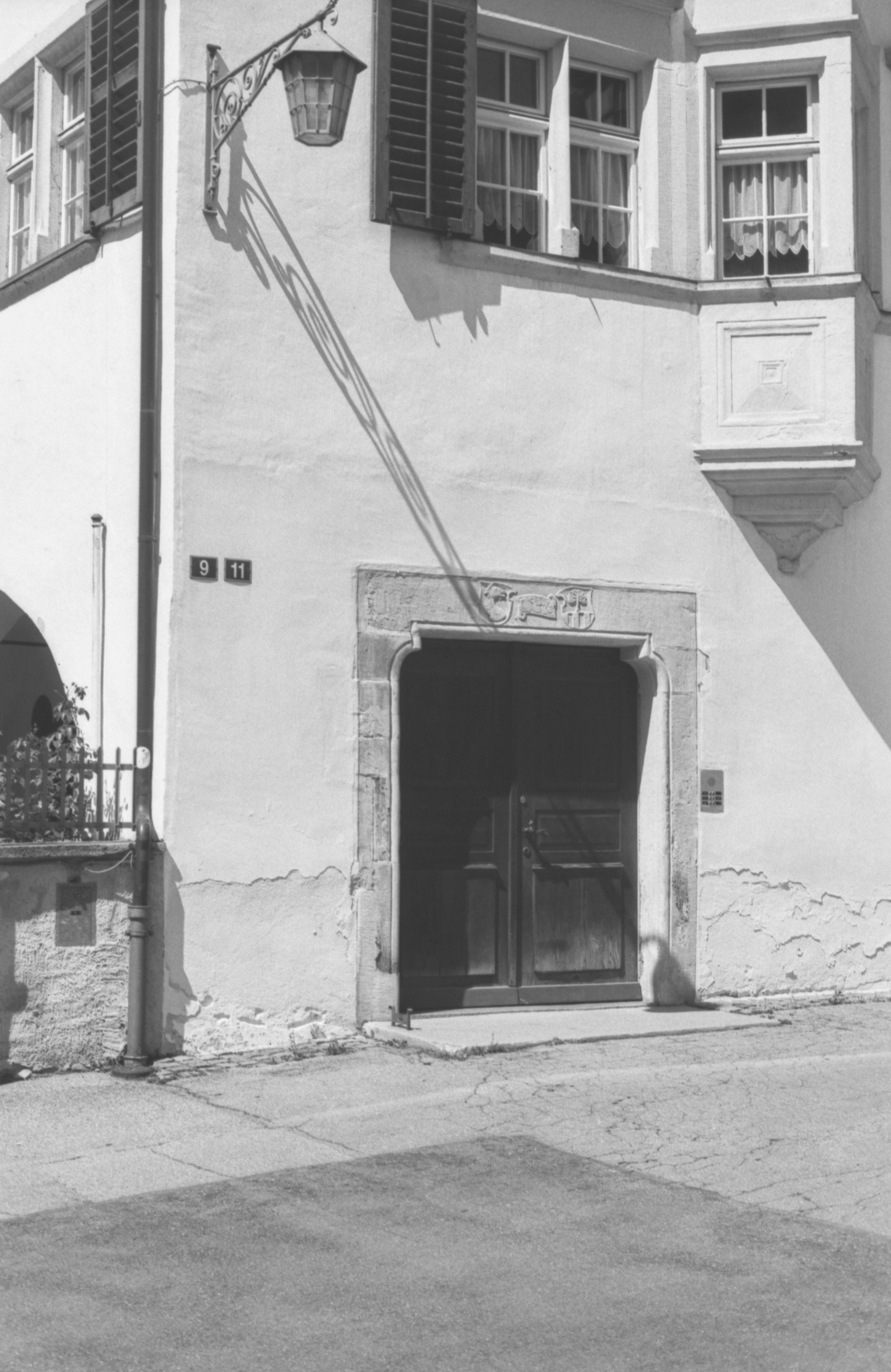 Facciata dell'edificio illuminata dal sole con lampade, porta e ombre ornate.