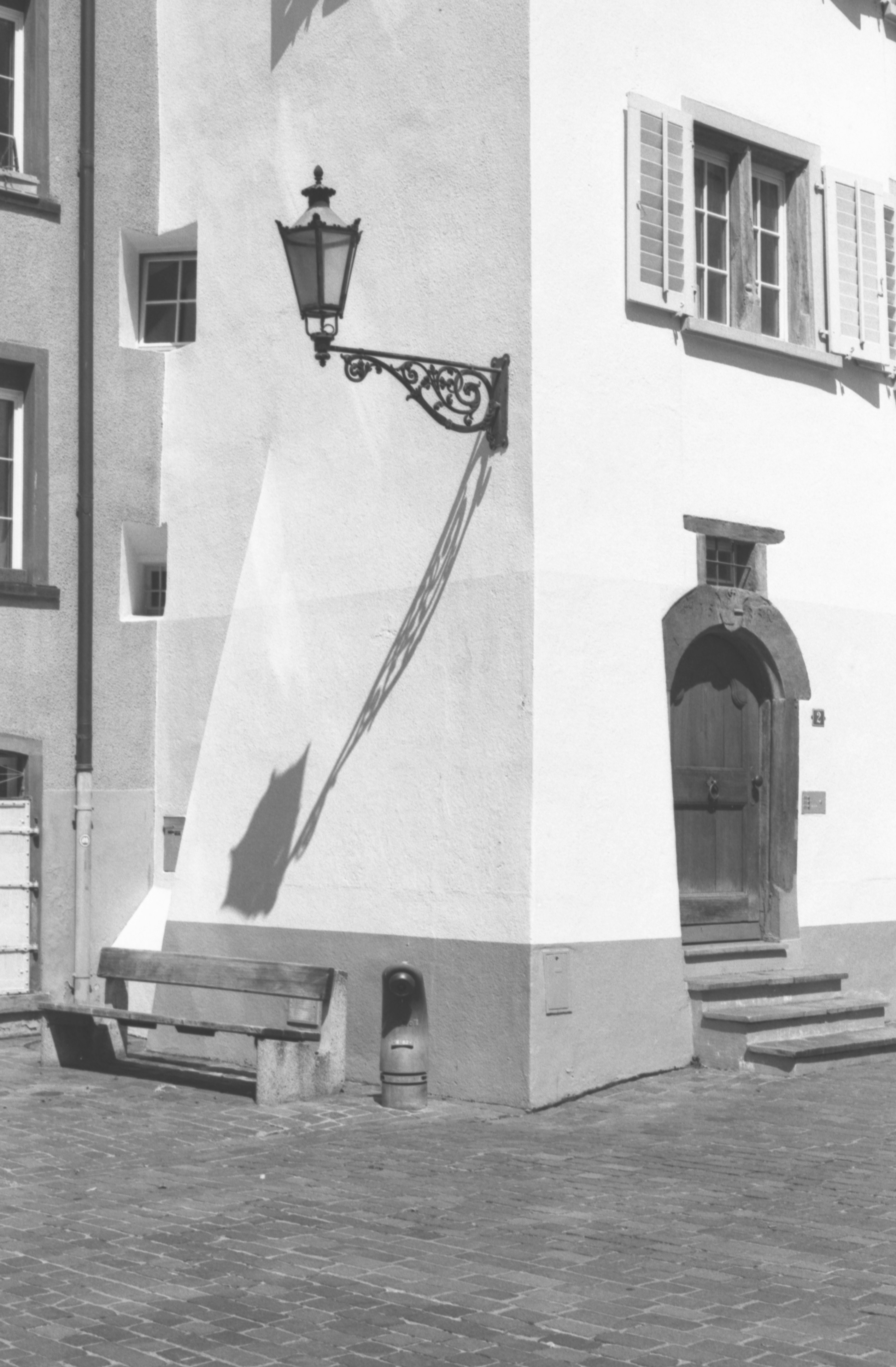 Angolo dell'edificio in bianco e nero con lampione e panchina.
