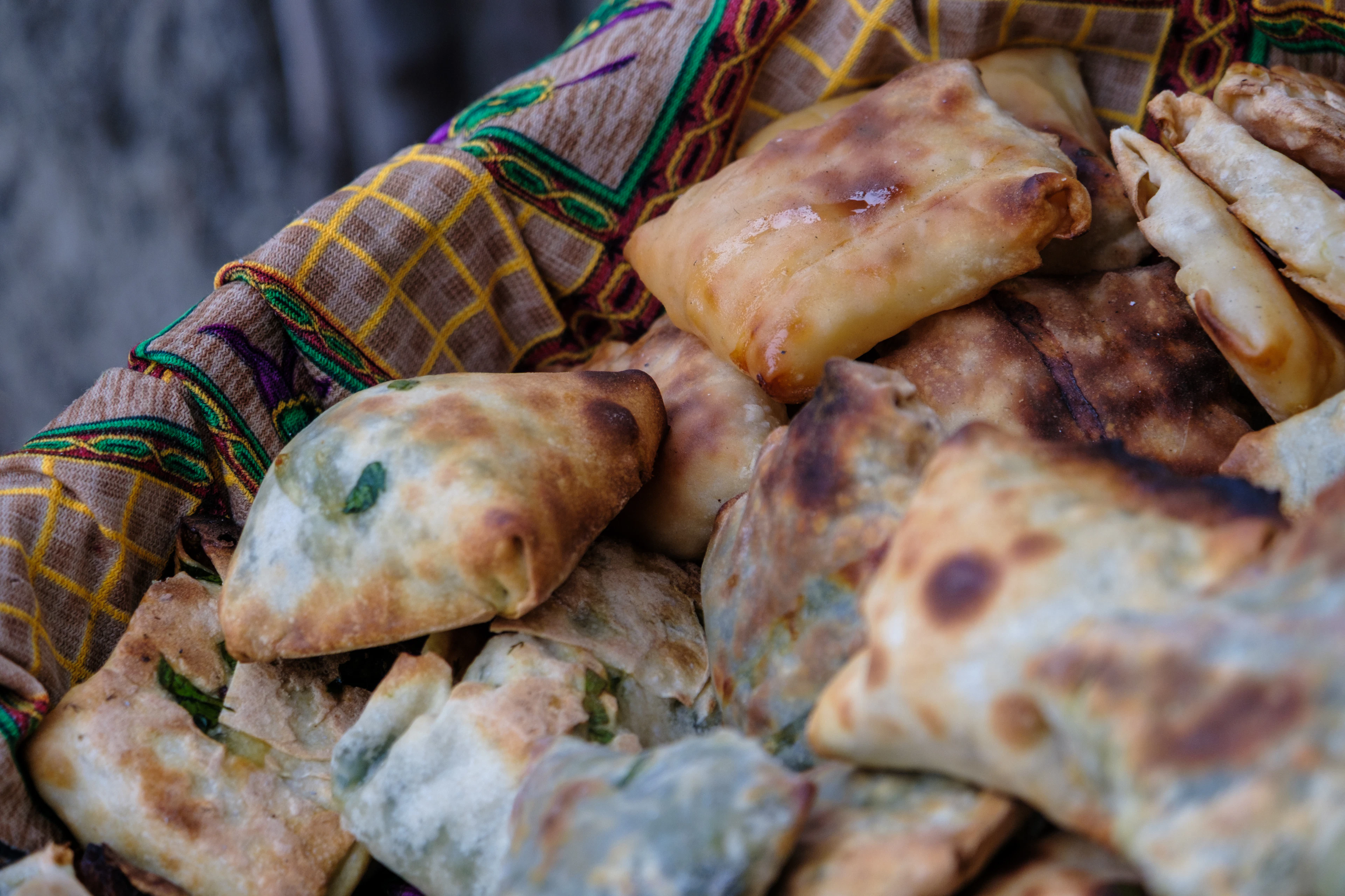 A basket lined with an embroidered Uzbek cloth heaped with freshly baked samsa, their pastry blistered gold and burst open to show a bright green herb filling.