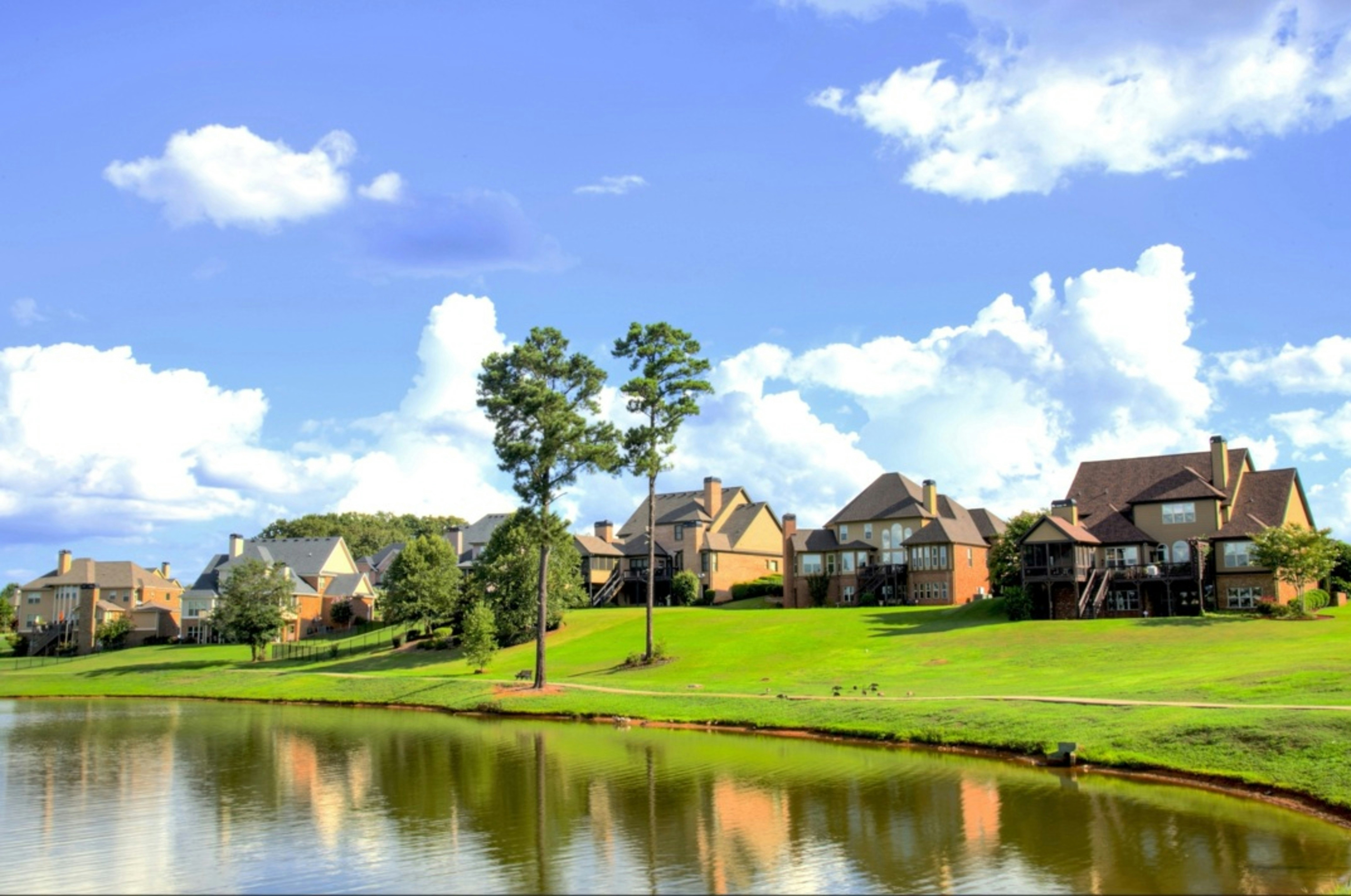 Open grass lot sloping down to a neighborhood pond, with homes along the far rise