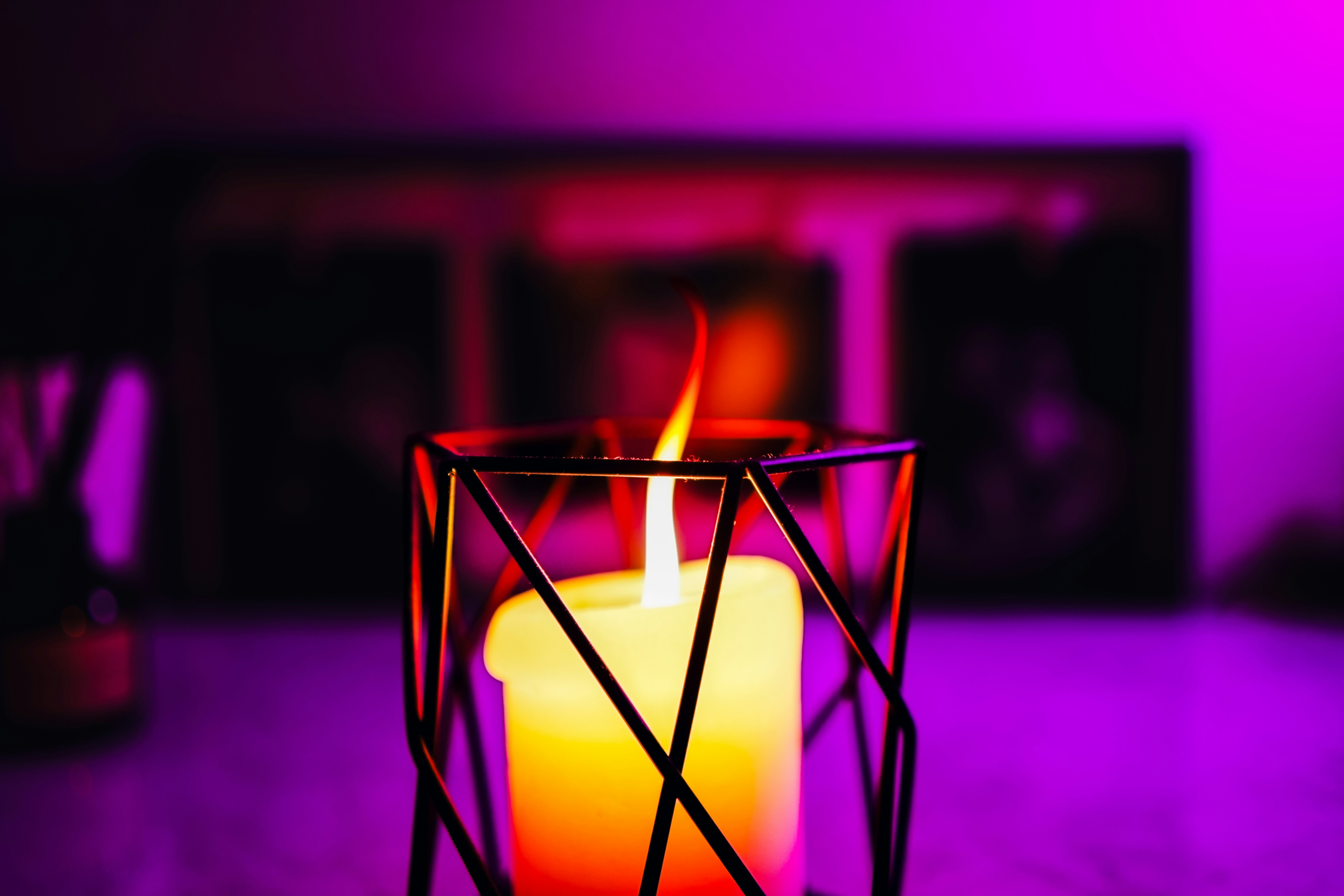 A lit candle in a geometric holder with purple lighting