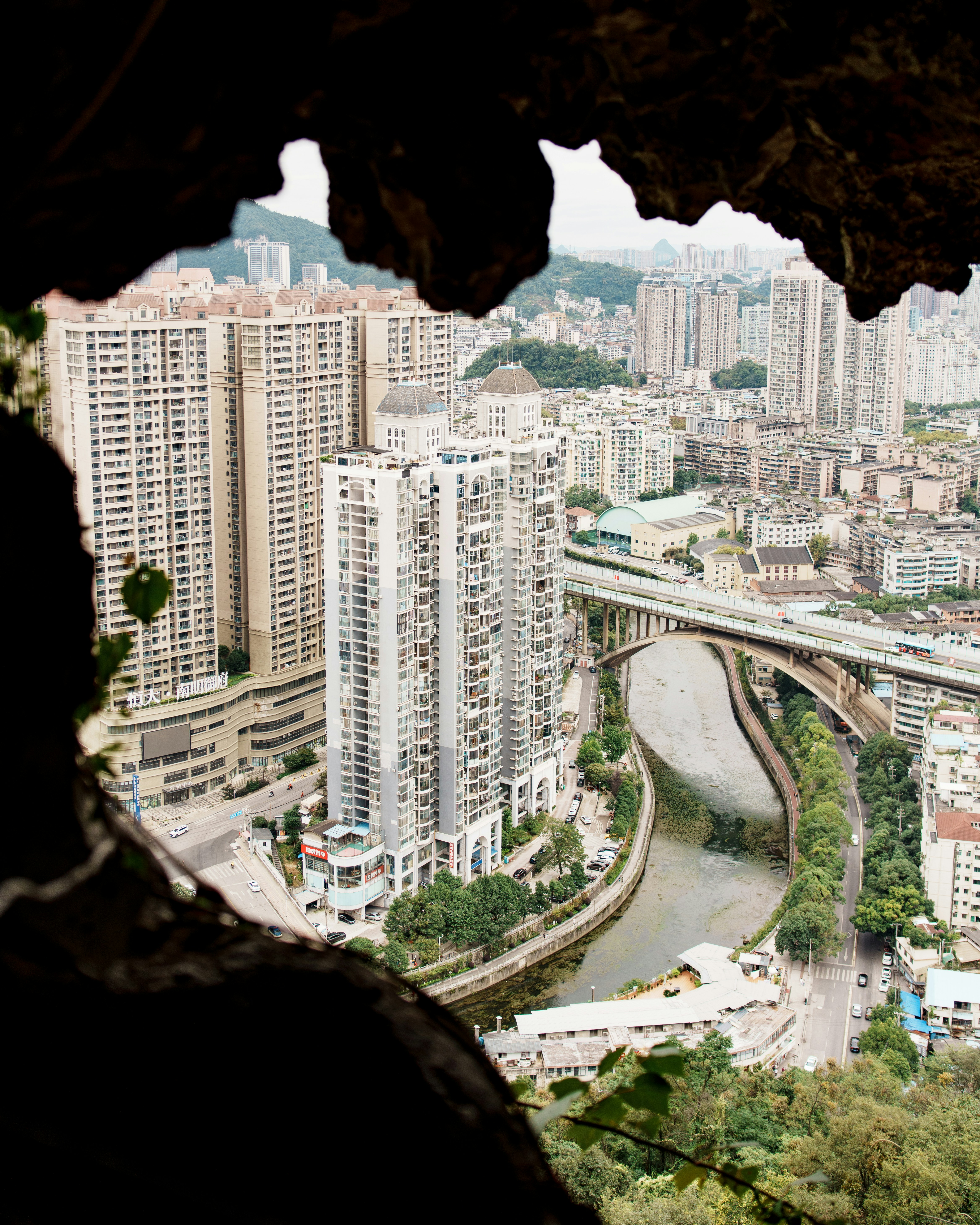 Cityscape with buildings, river, and bridge framed by cave opening.