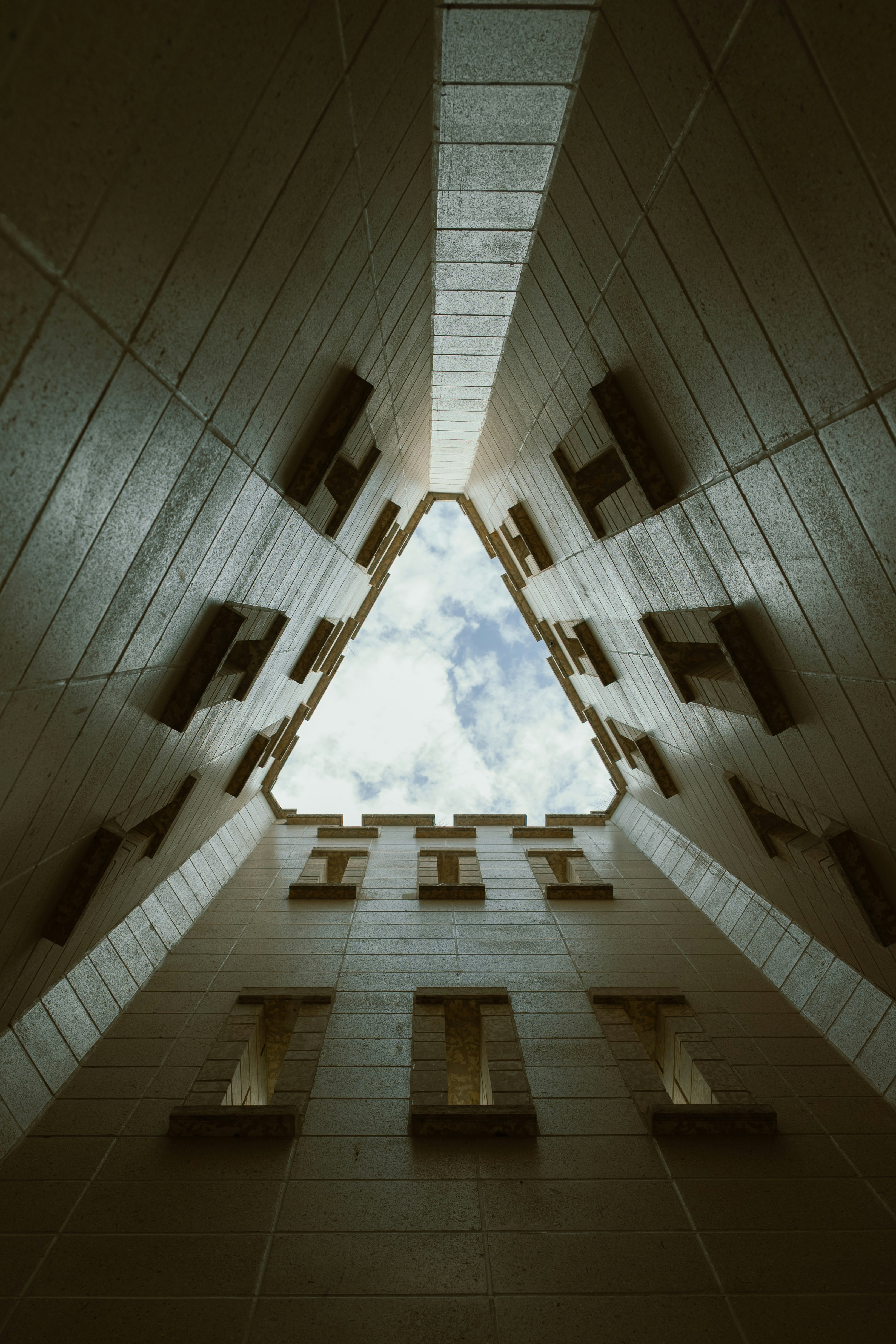 Looking up a triangular building shaft towards a cloudy sky.