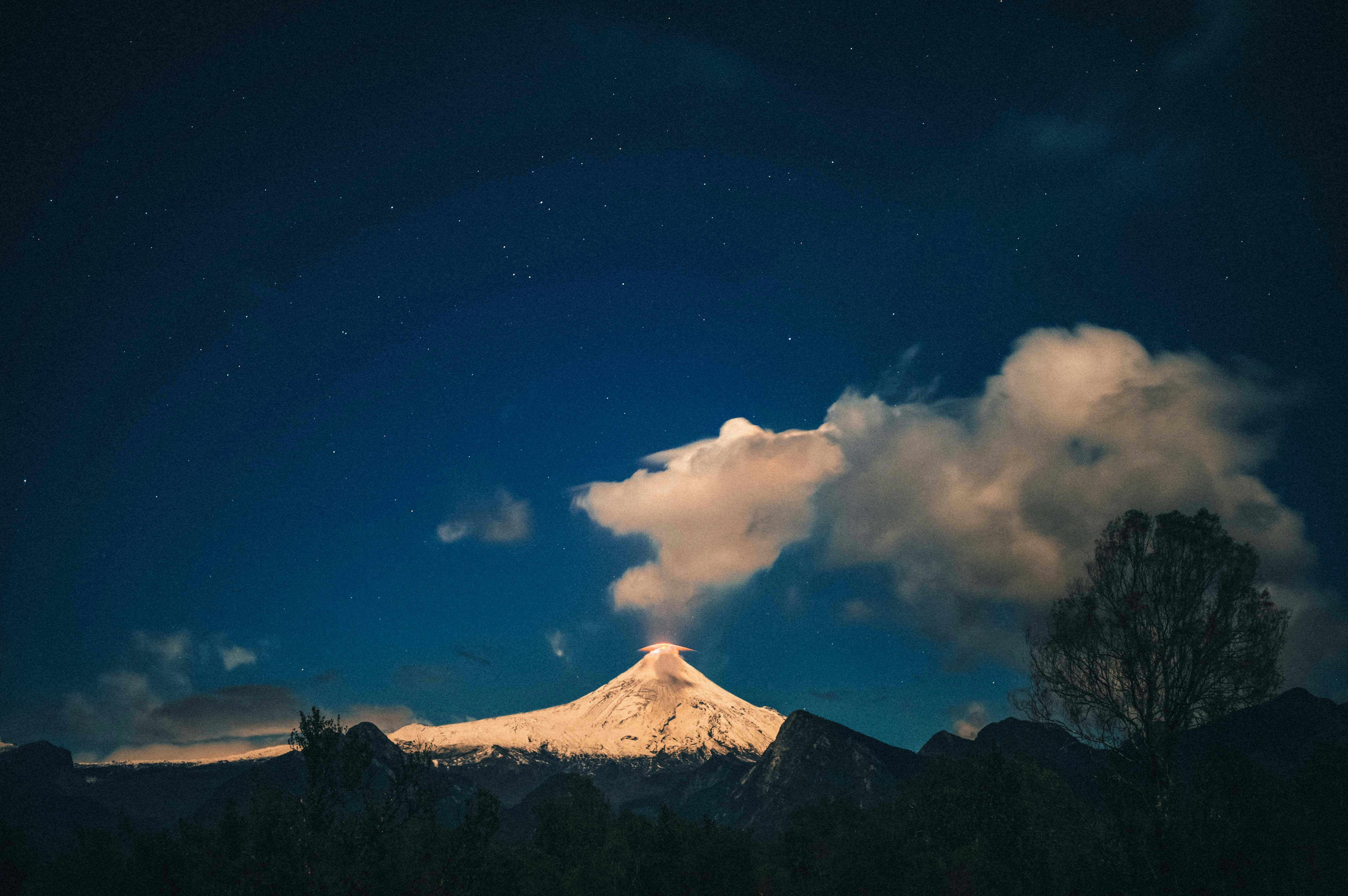 A snow-capped mountain under a starry night sky with clouds.