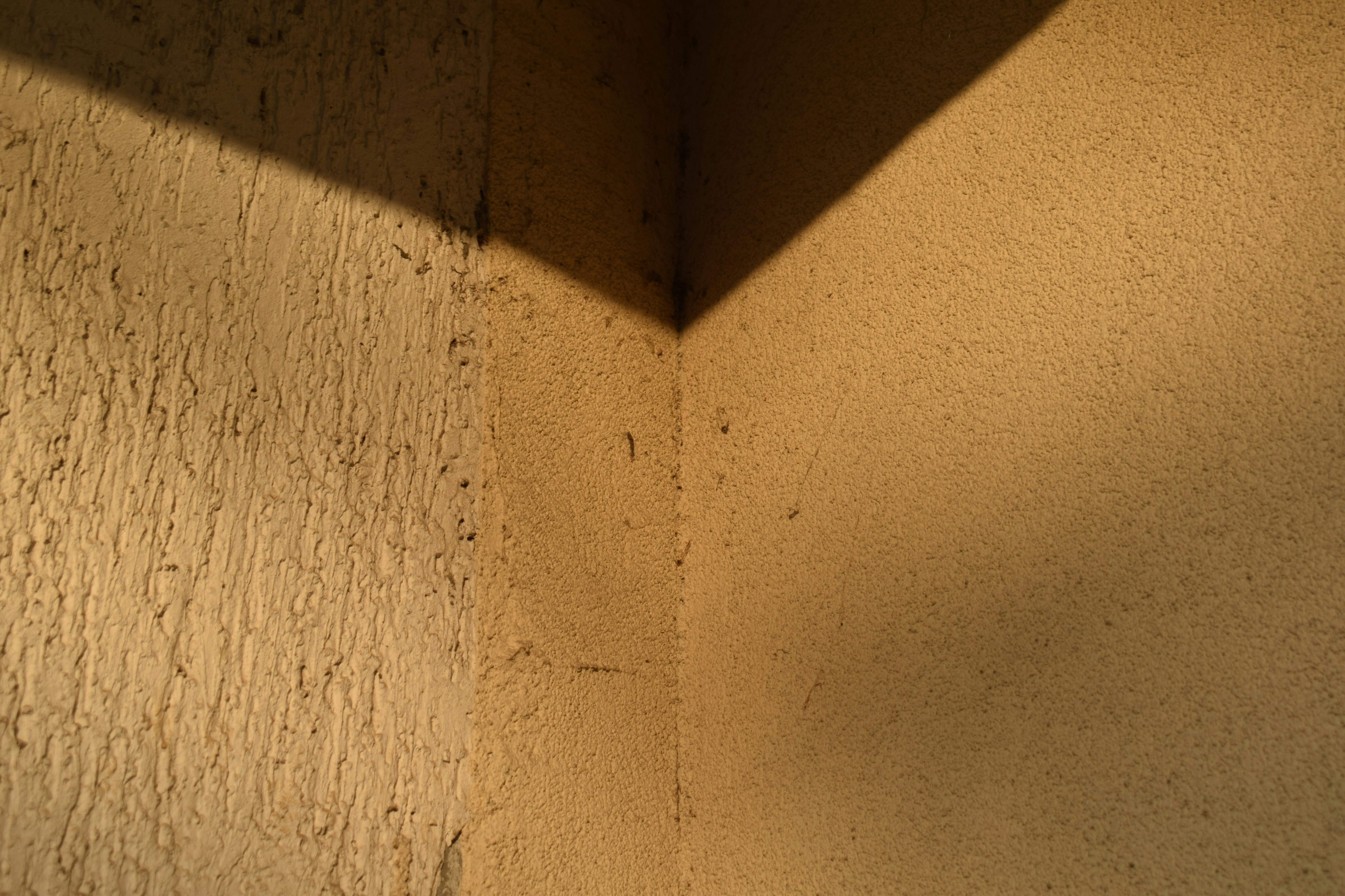 Textured light brown wall corner with a sharp diagonal shadow.