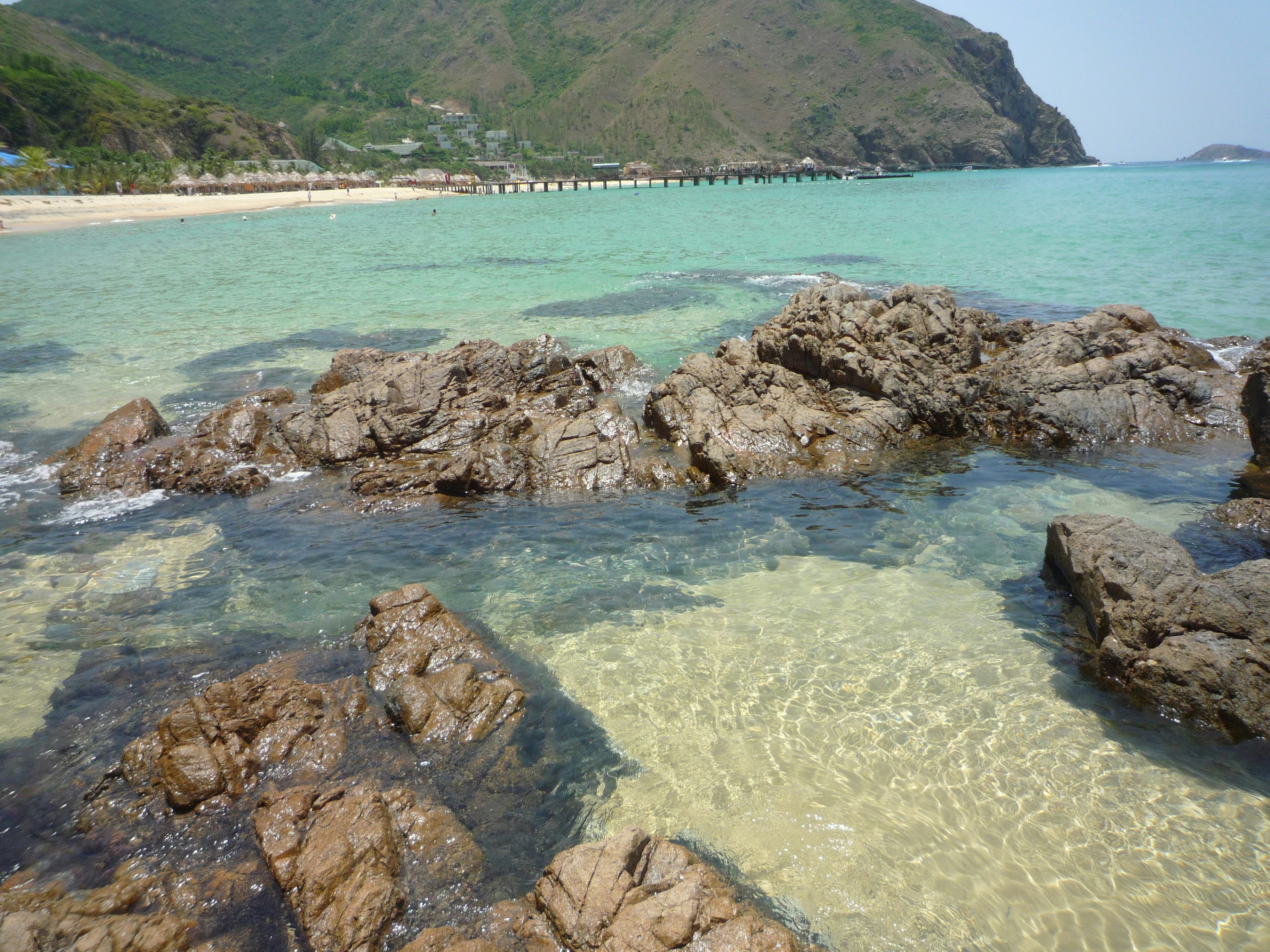 Clear turquoise ocean water with rocks and a sandy beach.