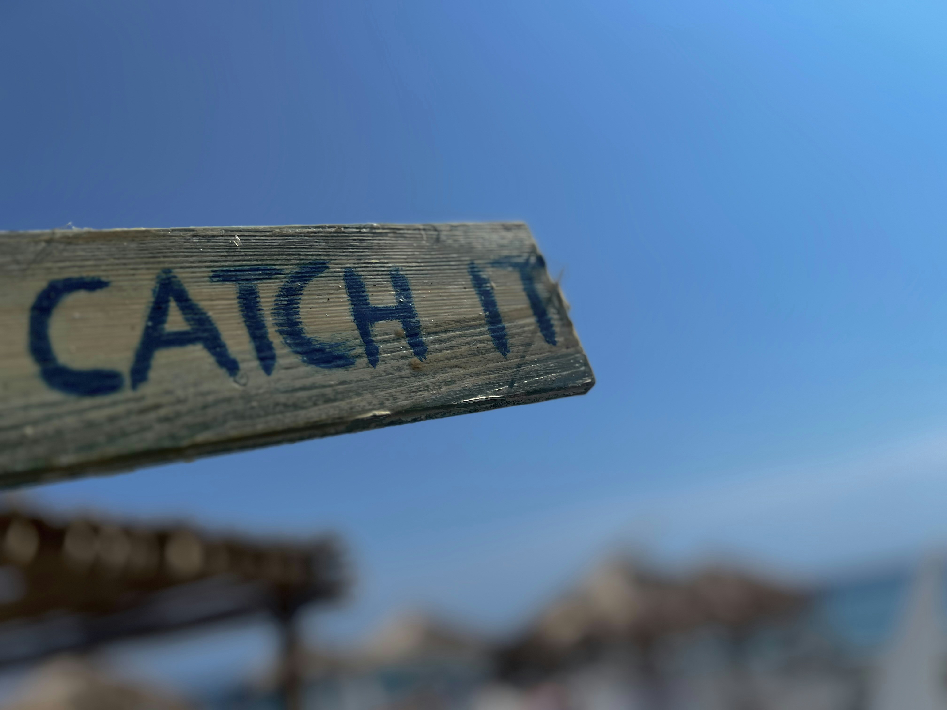 Weathered wooden sign with "catch it" against blue sky.