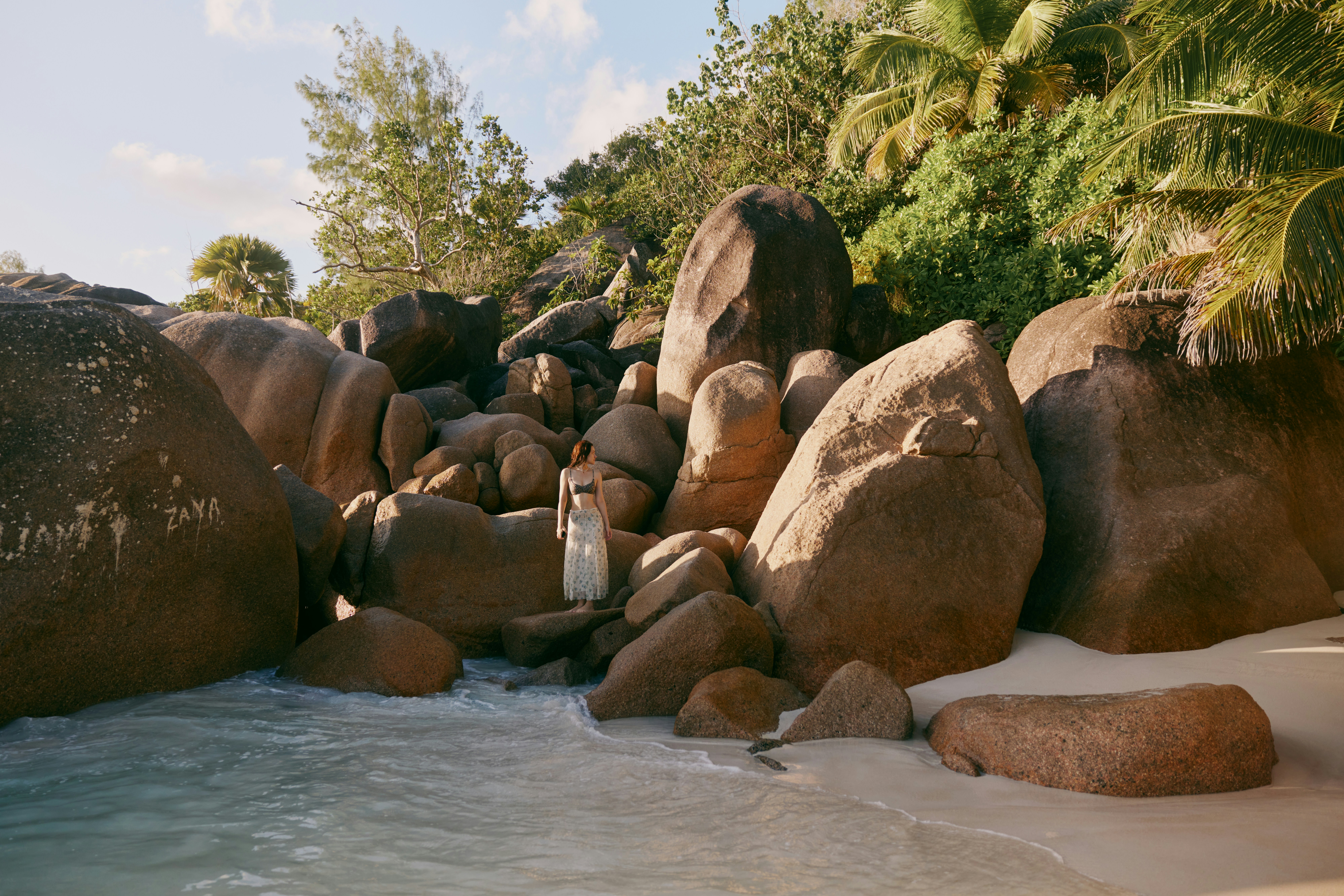 Woman among large boulders on a tropical beach