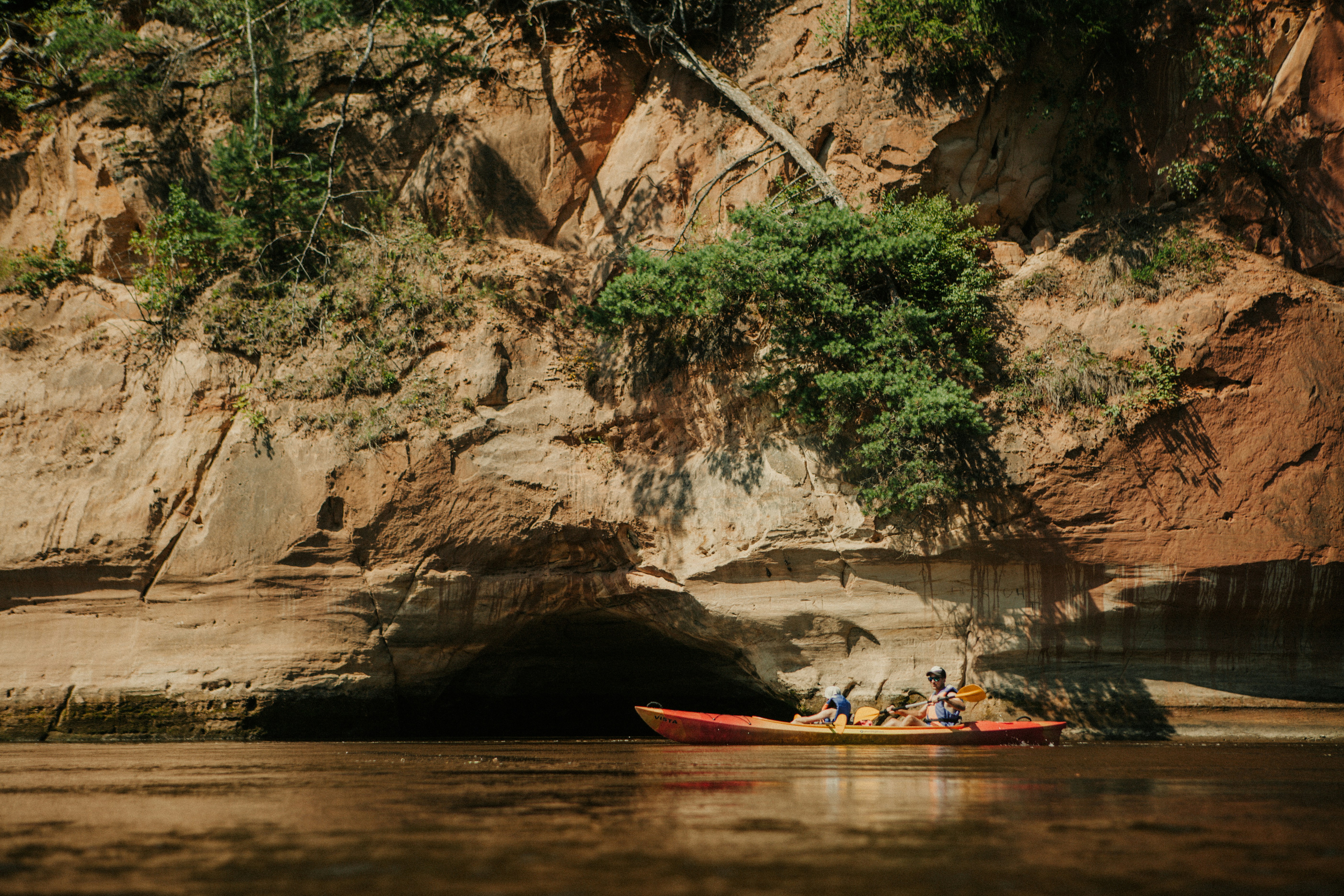 Kayak with people floating on a river near rocky cliffs.