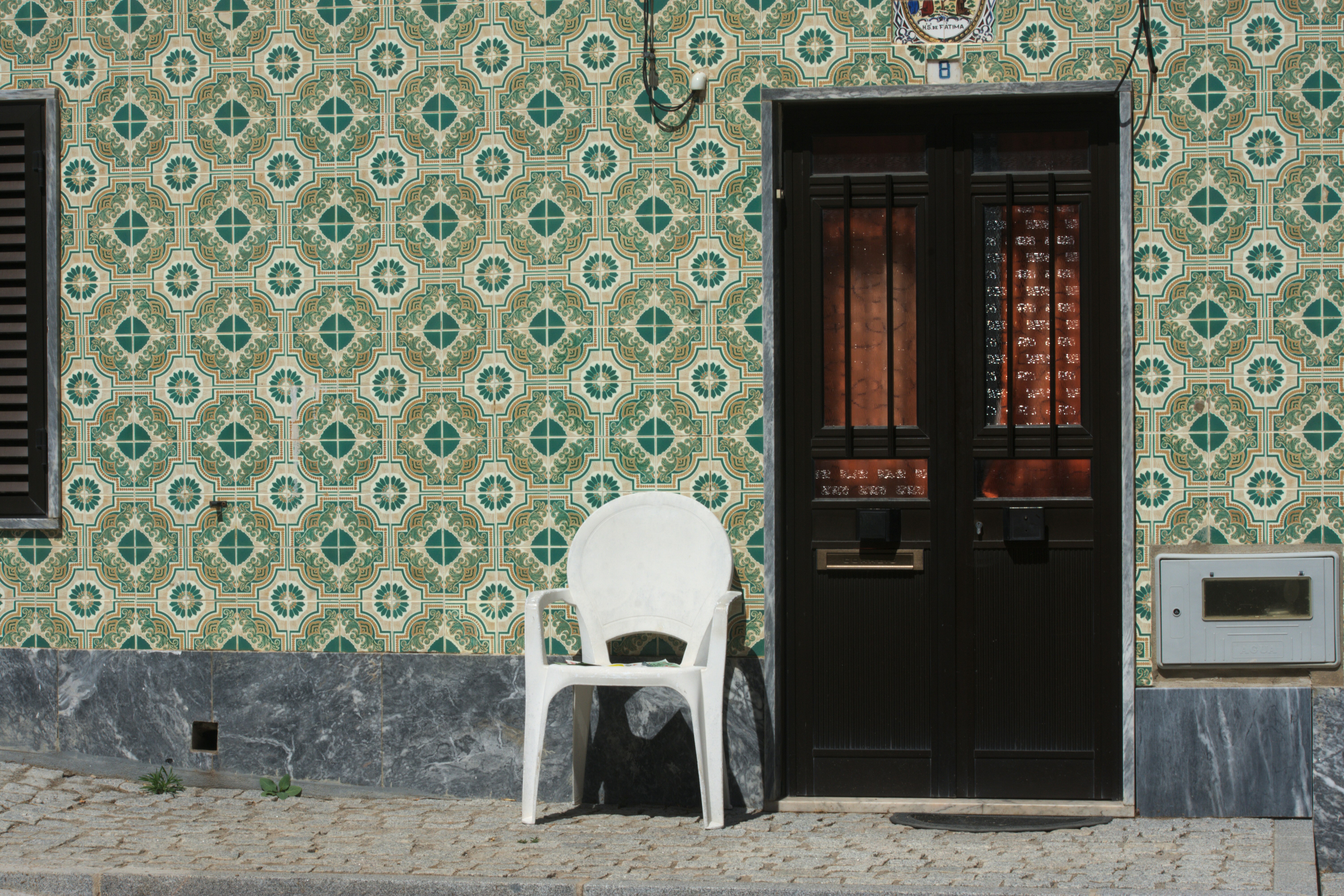 Patterned tiled facade with dark door and white chair.