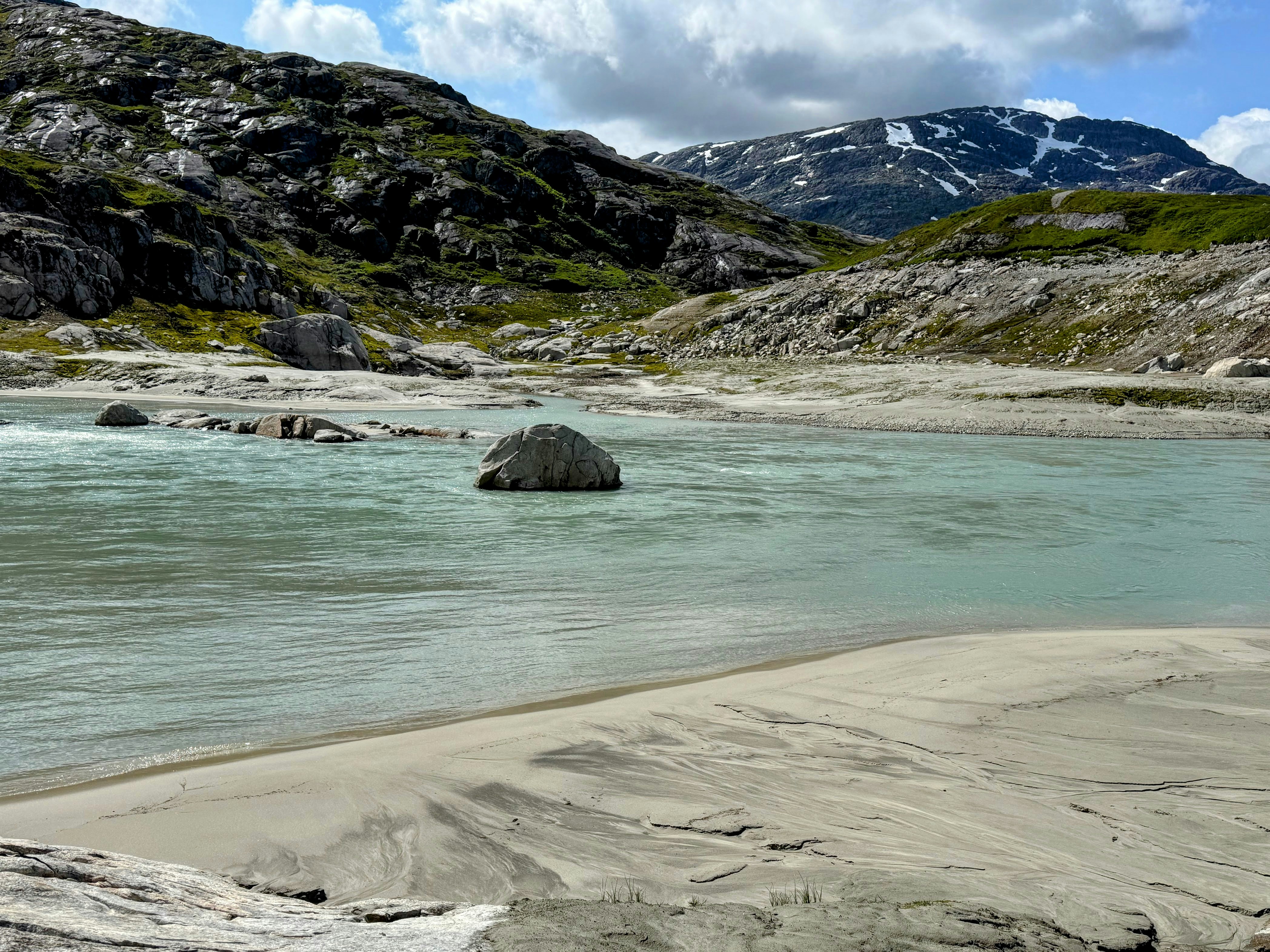 Serene river with sandy banks and rocky, snow-capped mountains.