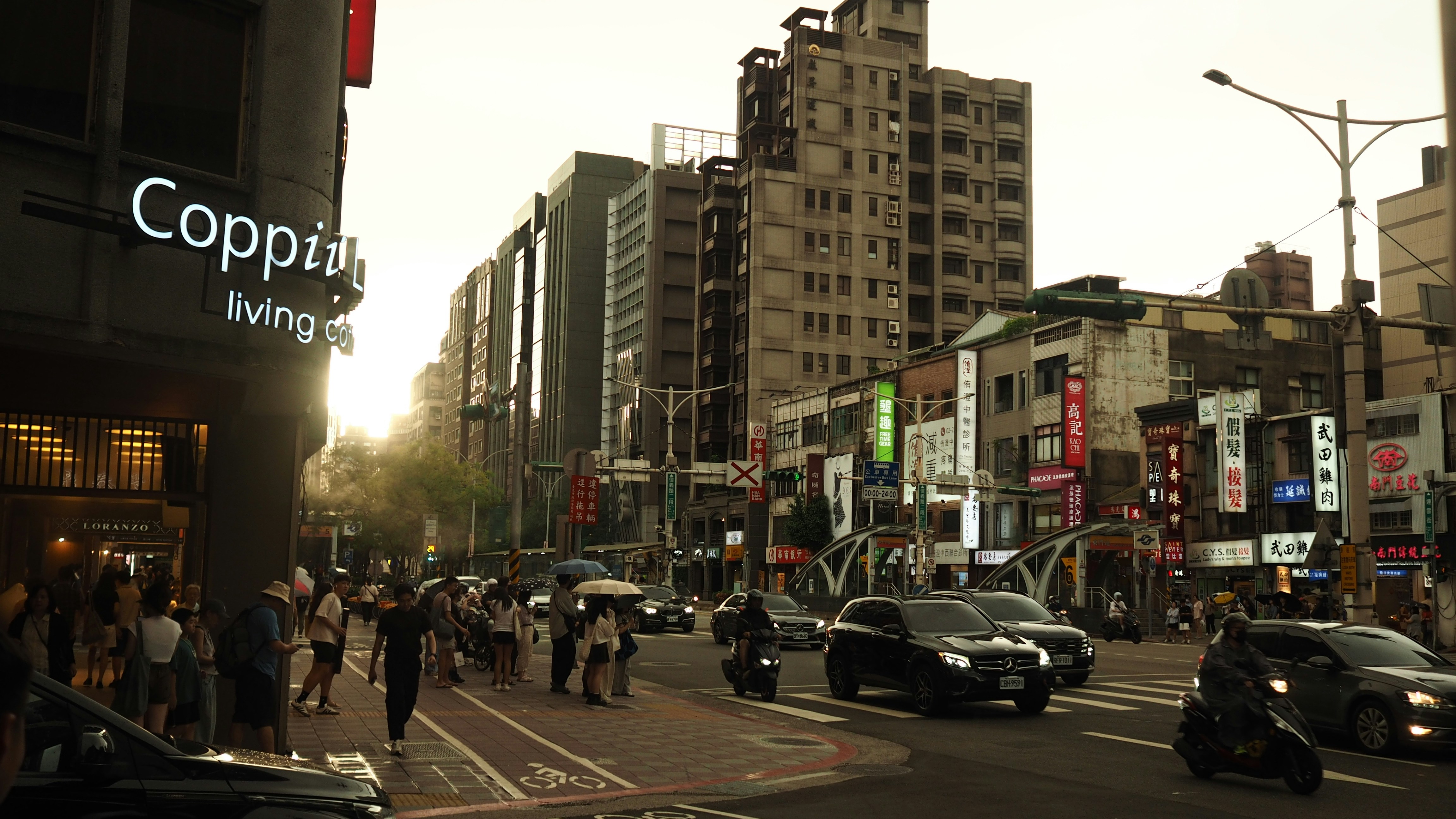Busy city street with pedestrians, cars, and buildings at sunset.