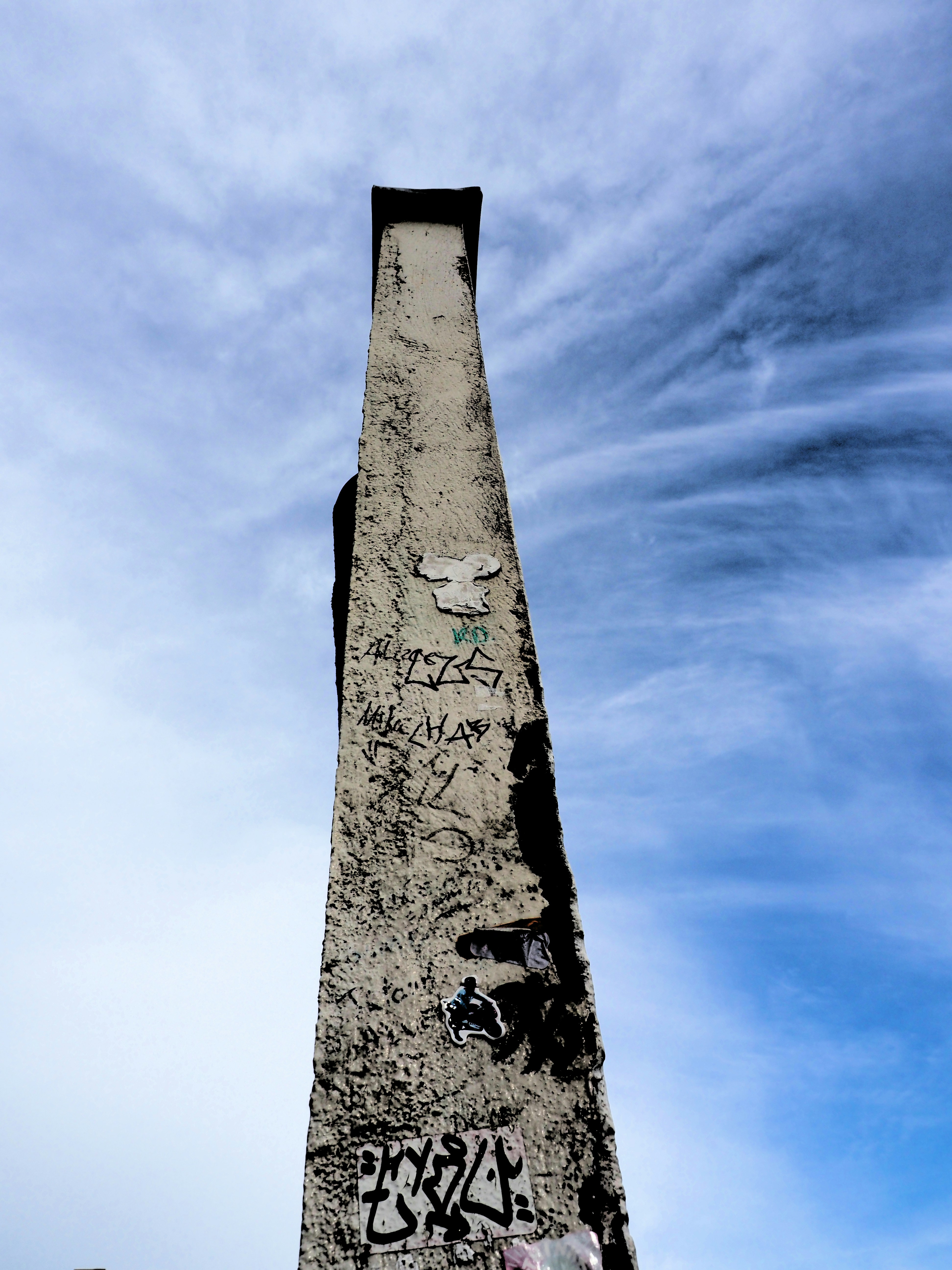 Graffiti-covered concrete pillar reaching towards a blue sky