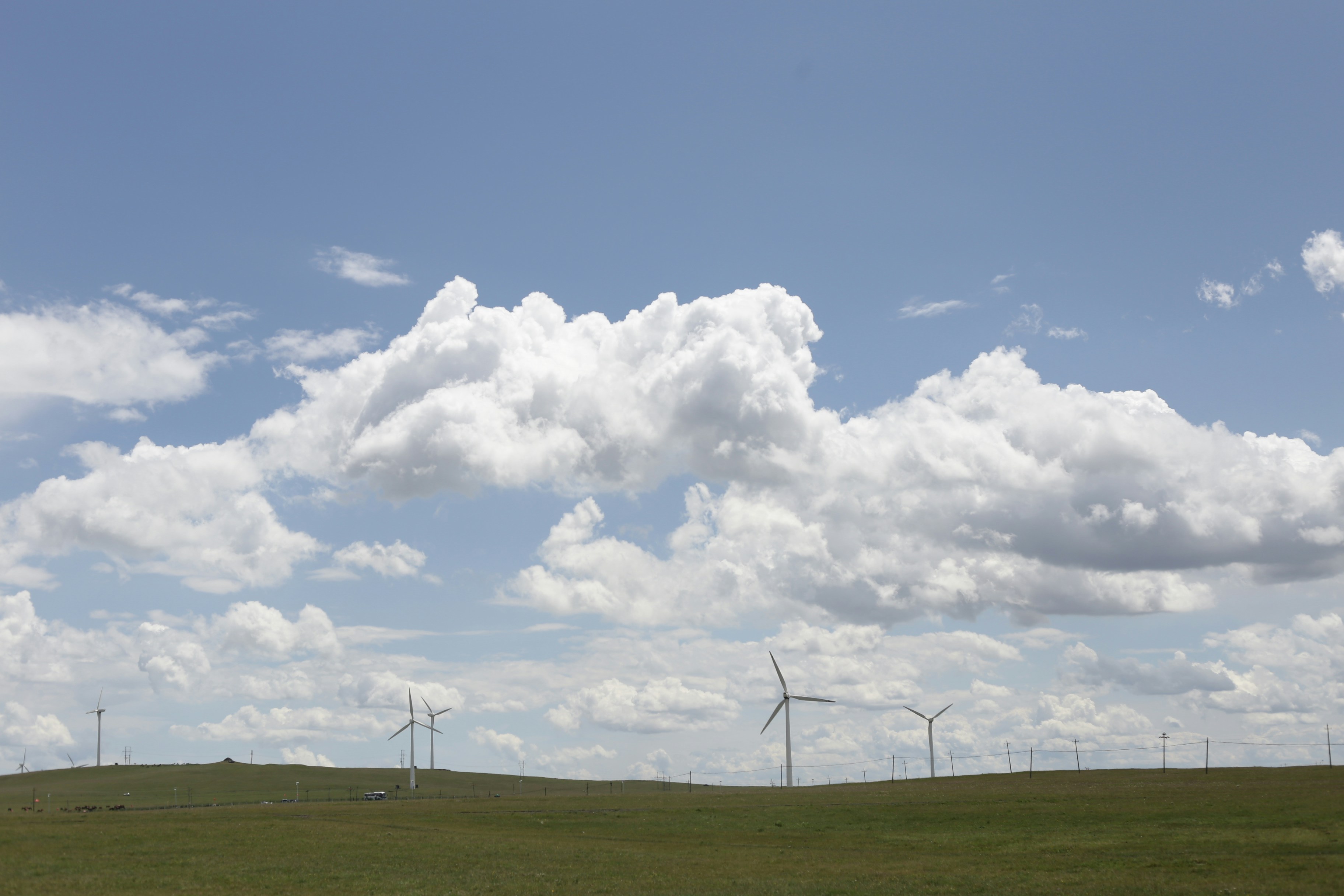 Wind turbines dot a green landscape beneath a cloudy sky.