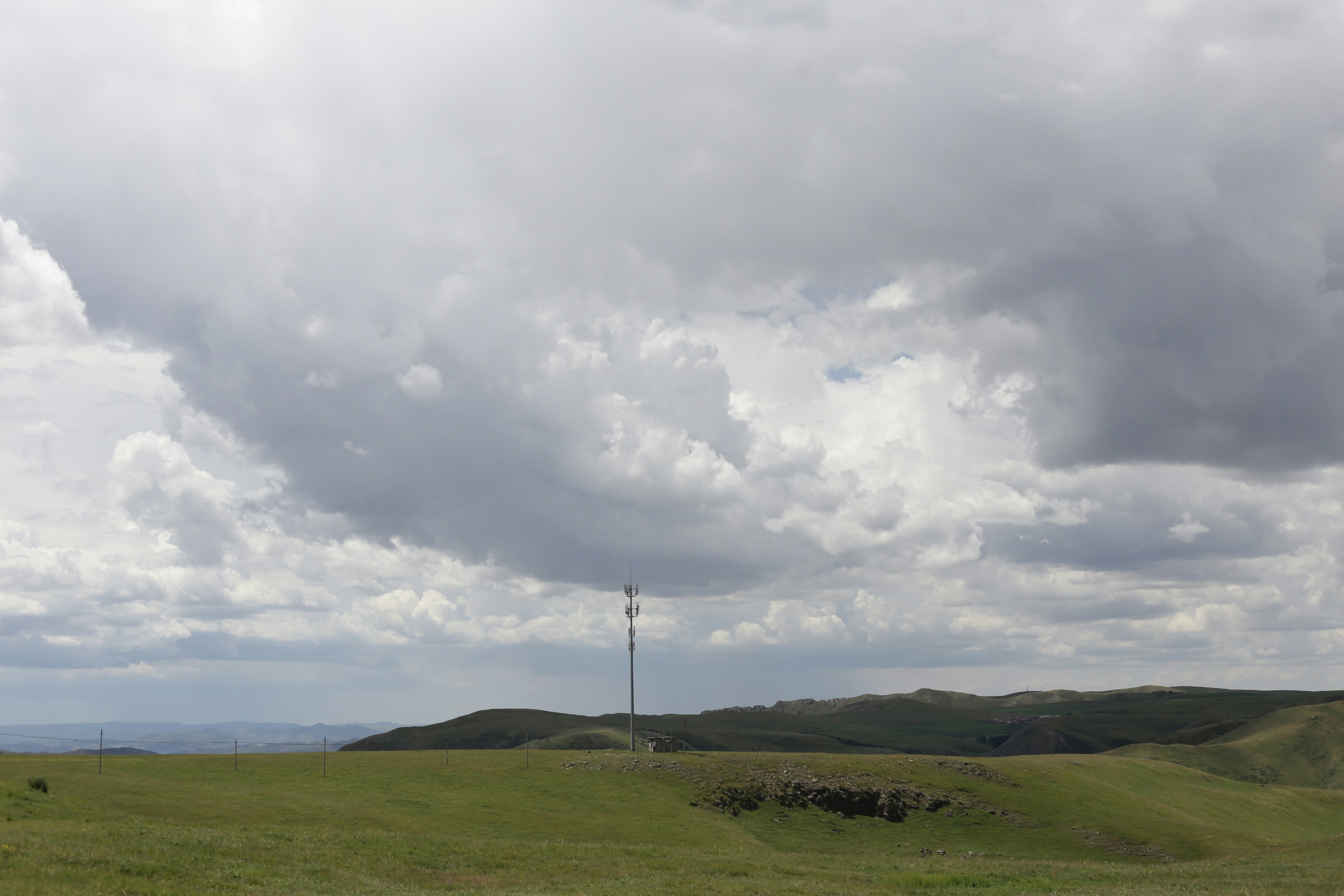 Green hills with a pole under a dramatic cloudy sky.