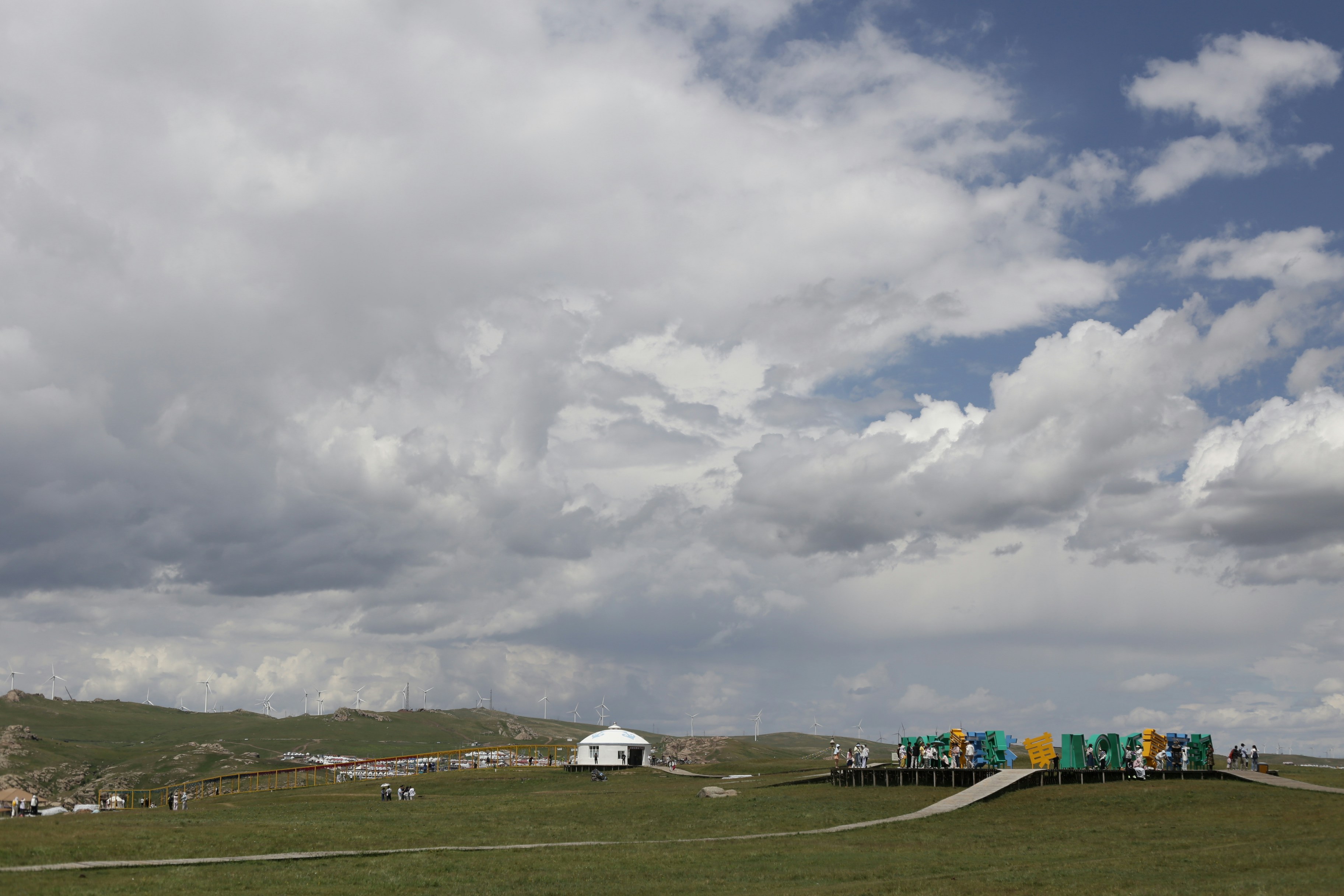 White yurt and colorful structures on a green grassy plain.